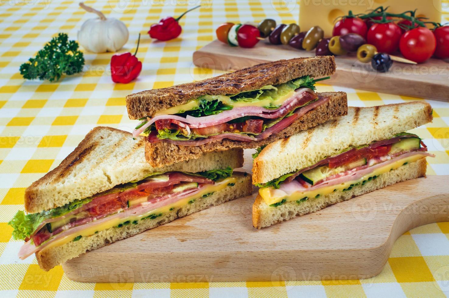 sándwich club con jamón, salami, ternera ahumada, queso, lechuga y rúcula.Preparación de sándwich tostado. foto