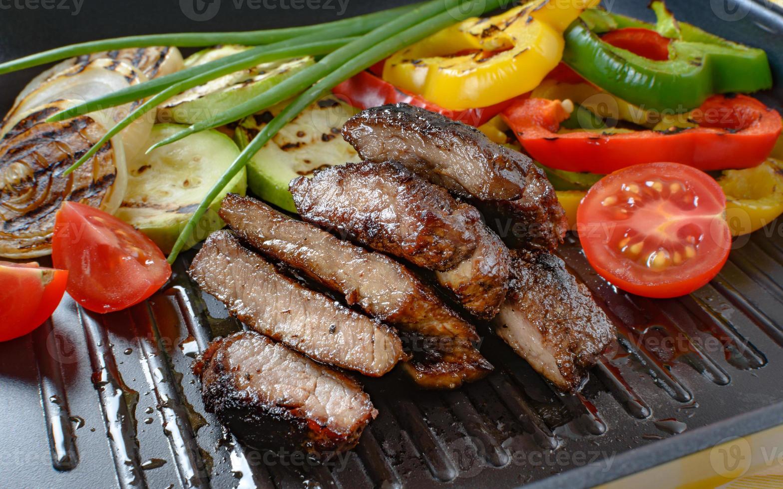 Grilled beef meat on grill with grilled vegetables in the background. photo