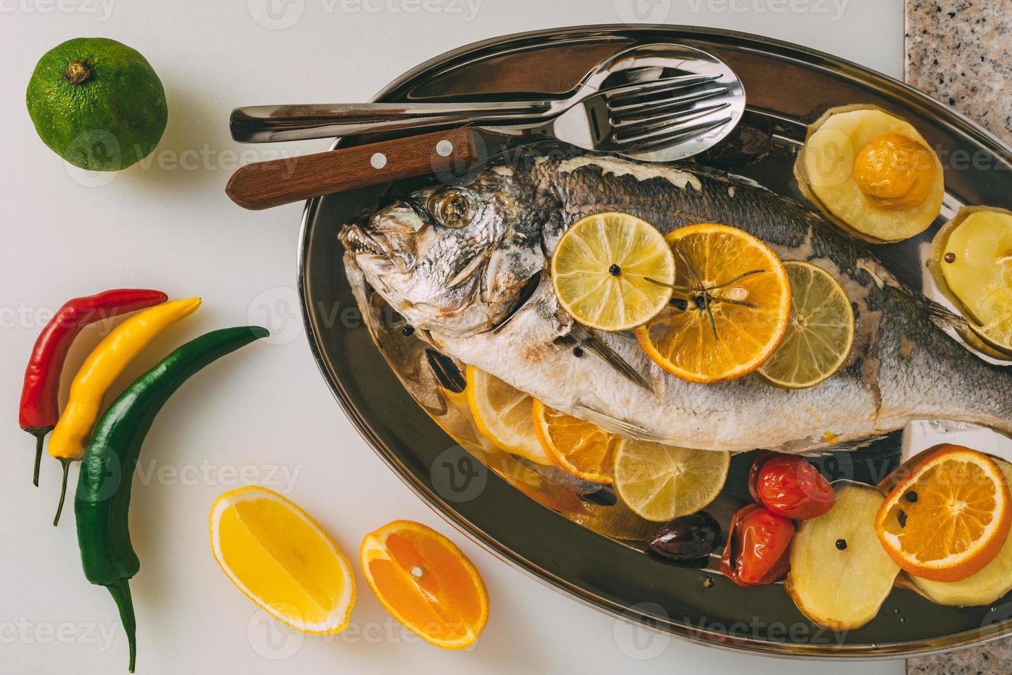 dorada pescado al plato al horno con patatas, romero, limón, naranja, aceitunas, tomates y lima. orata fresca, preparación de pescado dorade. foto