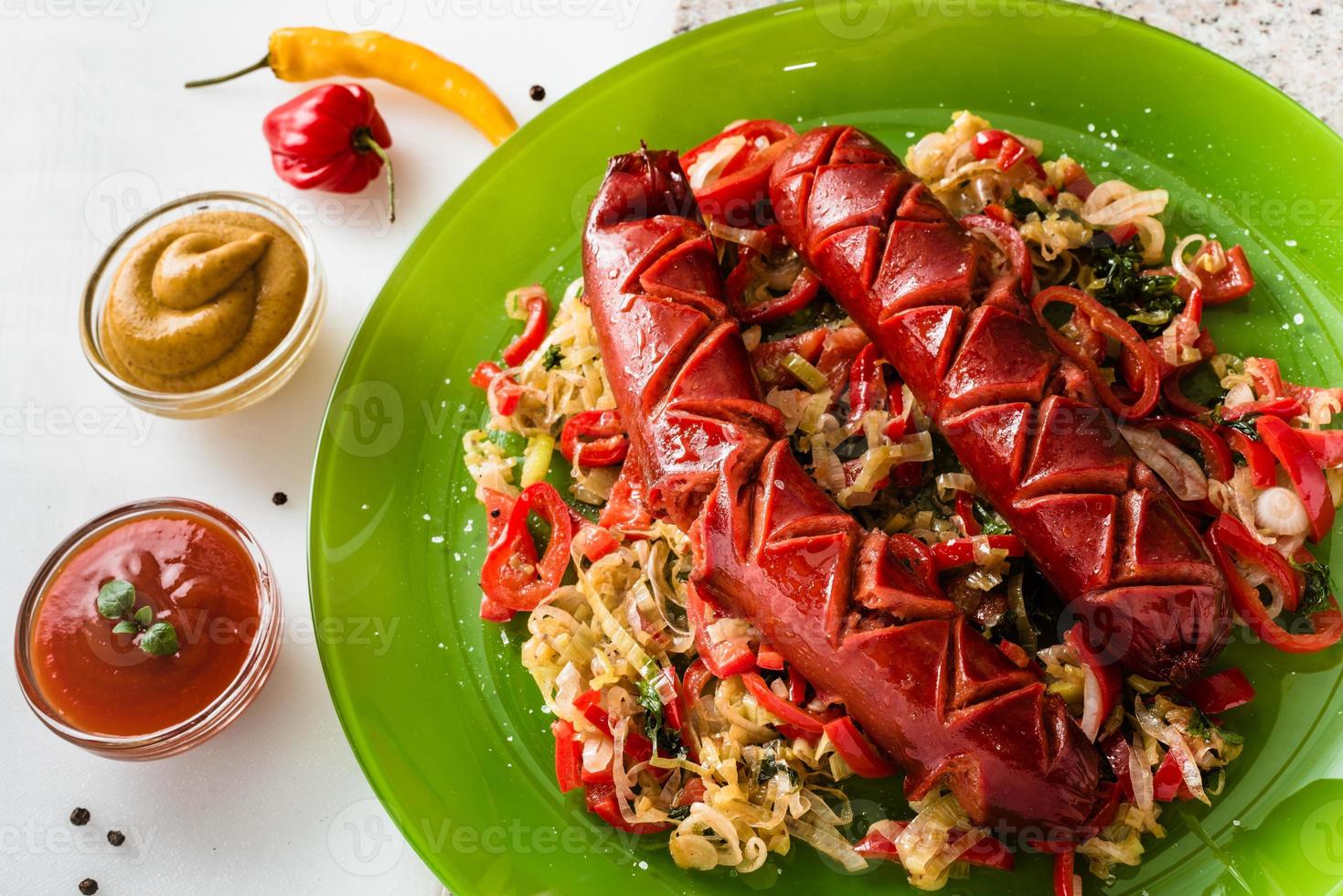 Sausage and mix of fresh vegetables served on a plate, mustard, ketchup, fresh hot chili peppers and herbs. photo