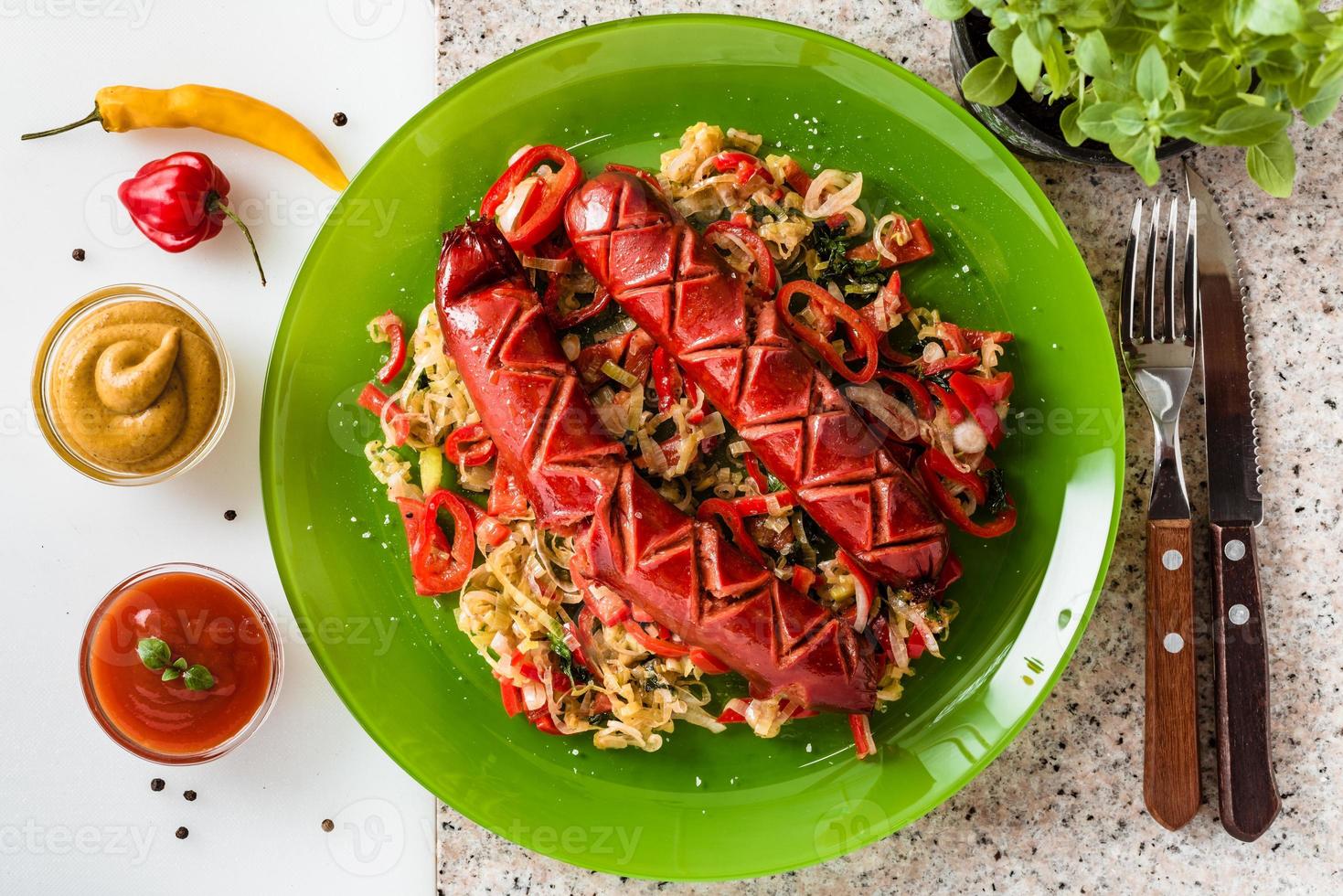 Sausage and mix of fresh vegetables served on a plate, mustard, ketchup, fresh hot chili peppers and herbs. photo