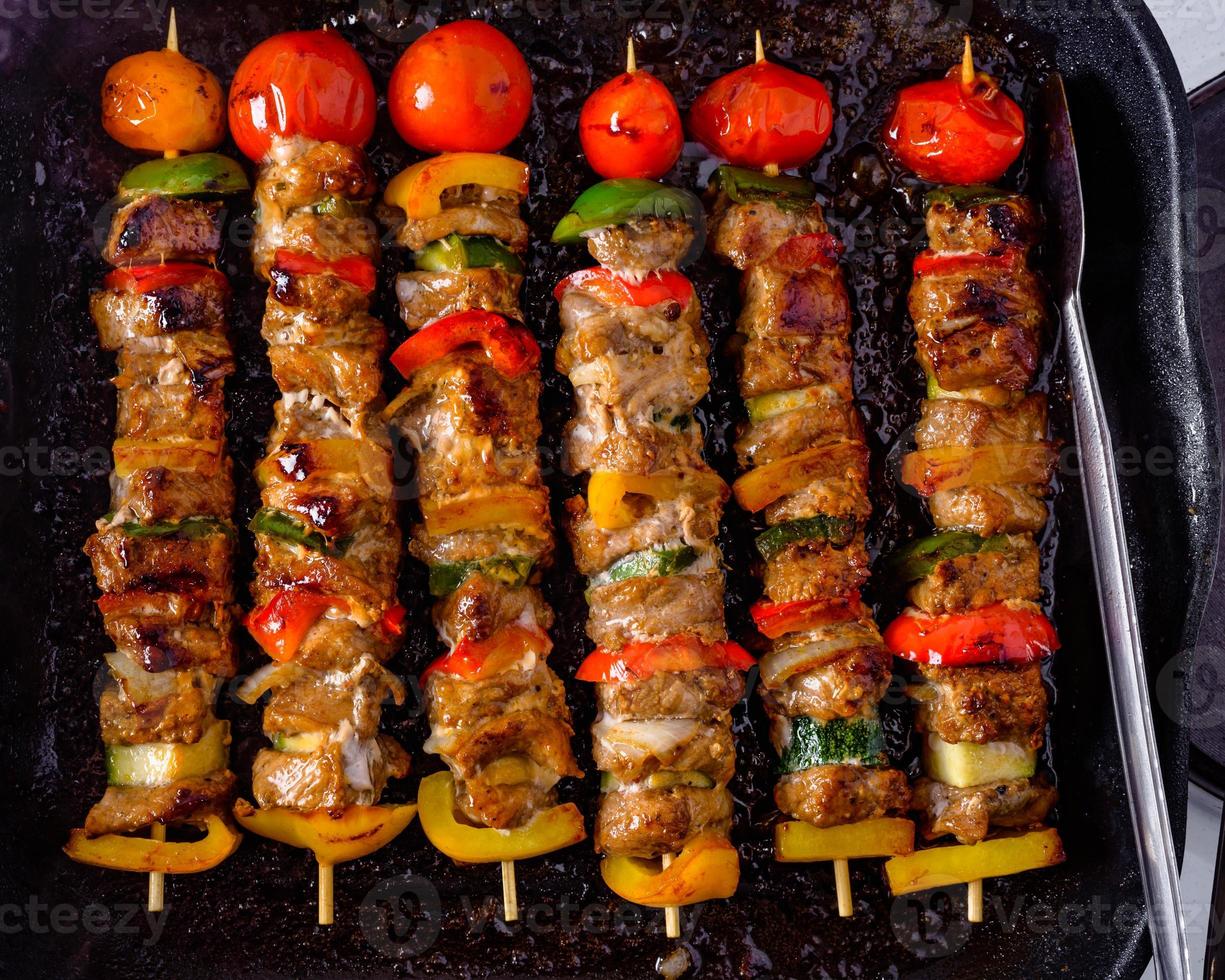 Grilled skewers on wooden sticks, pork meat and vegetables on grill. photo