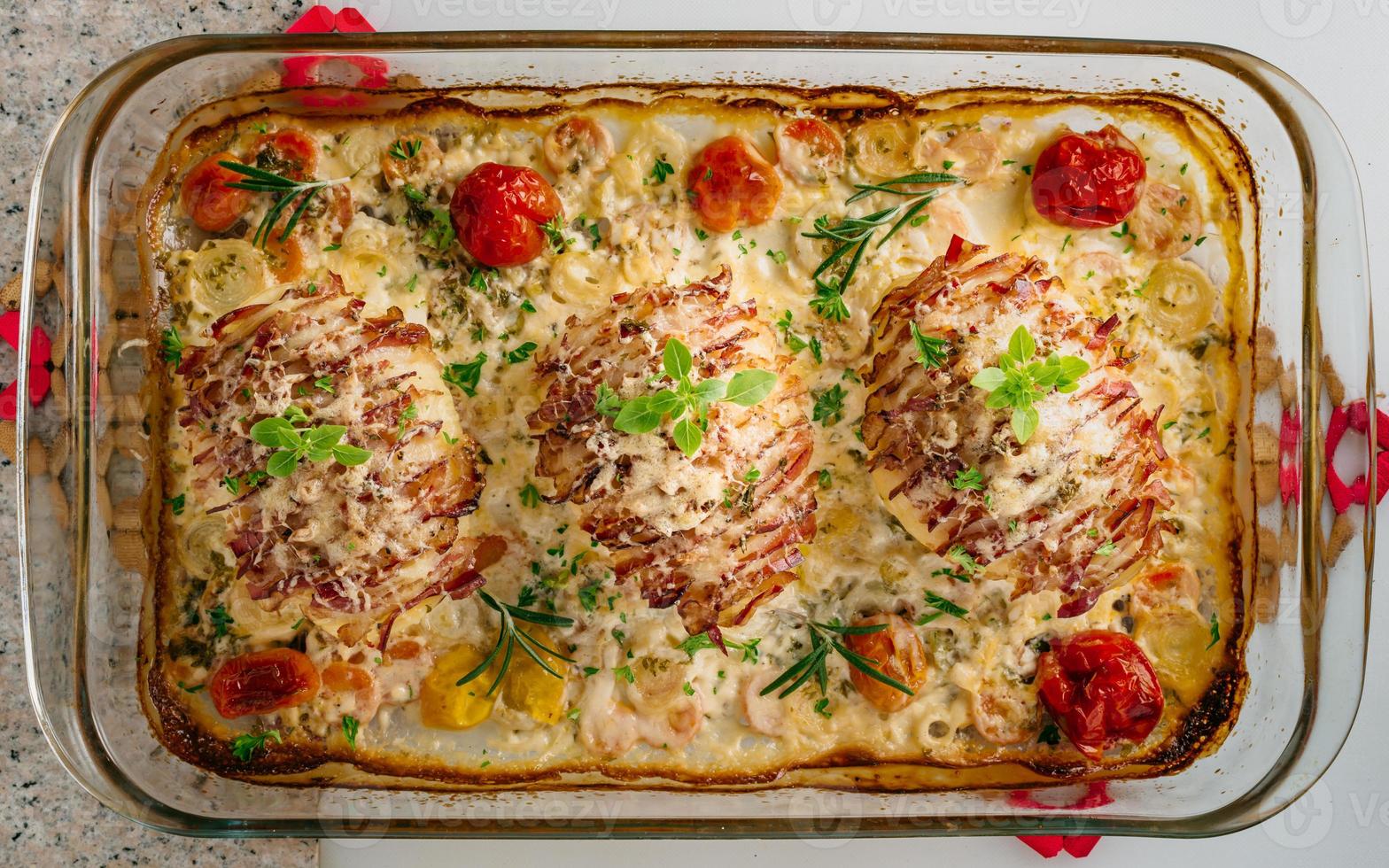 Potato filled with bacon baked in oven. Sour cream for cooking with carrot, tomato, onion, spices and herbs in baking dish. photo