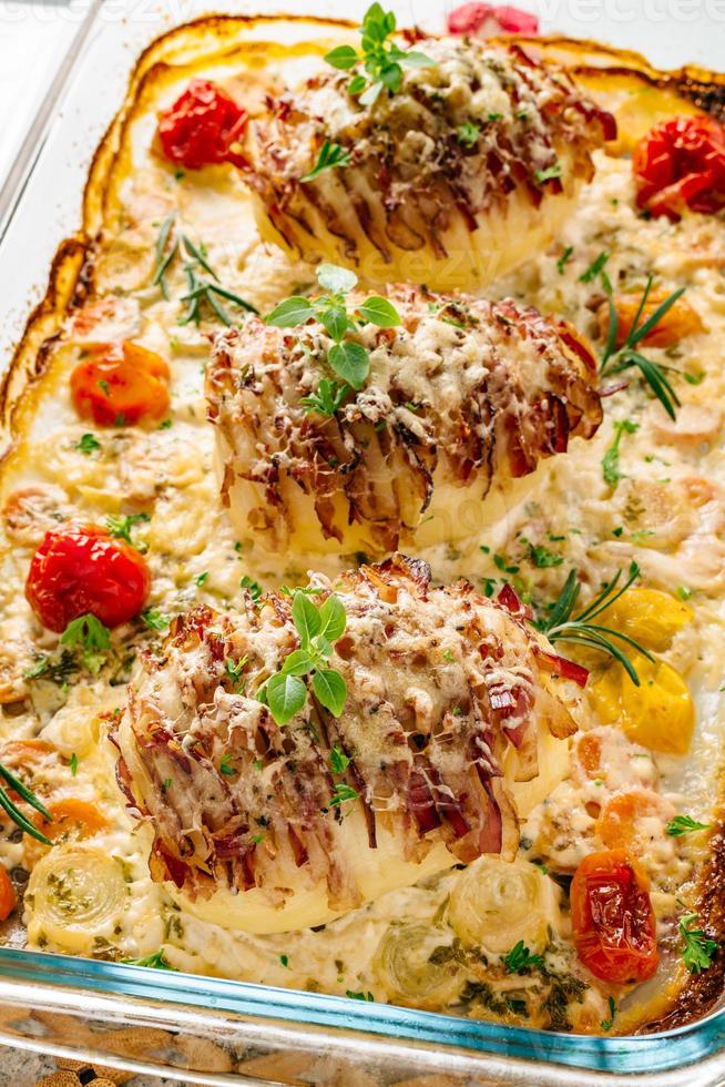 Potato filled with bacon baked in oven. Sour cream for cooking with carrot, tomato, onion, spices and herbs in baking dish. photo