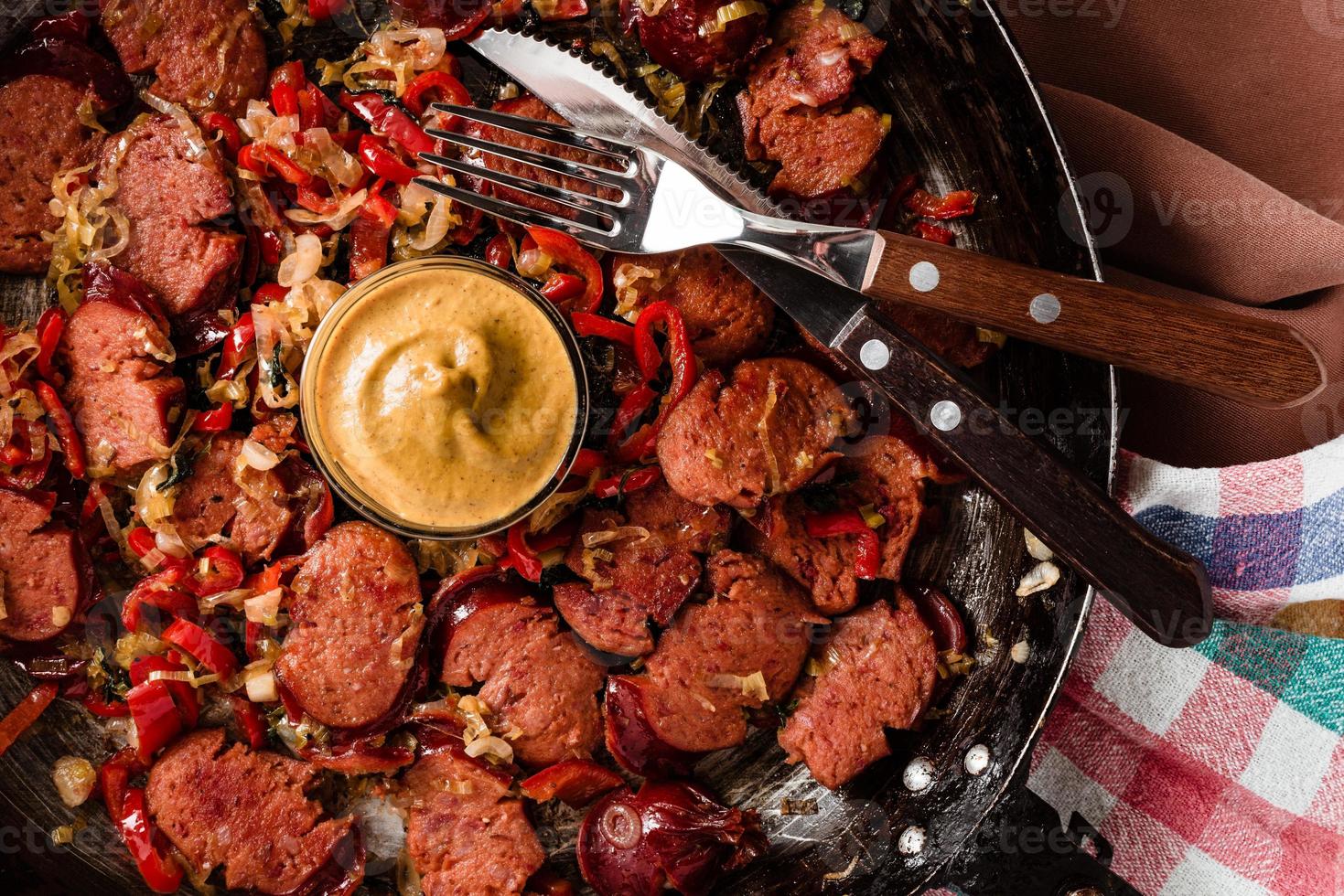 Sliced sausage and mix of fresh vegetables fried in the rustic pan with mustard on dishcloth. photo