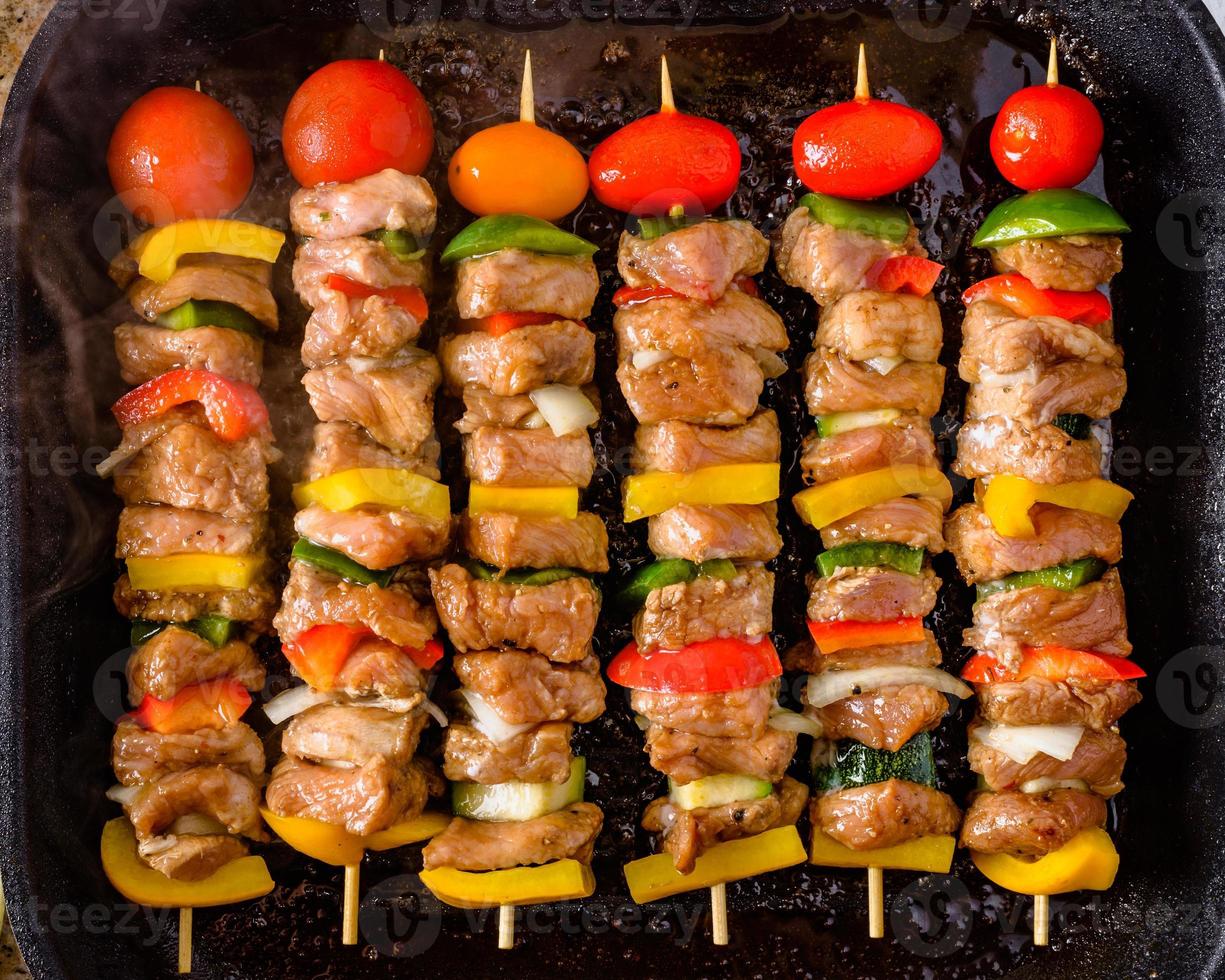 Grilled skewers on wooden sticks, pork meat and vegetables on grill. photo
