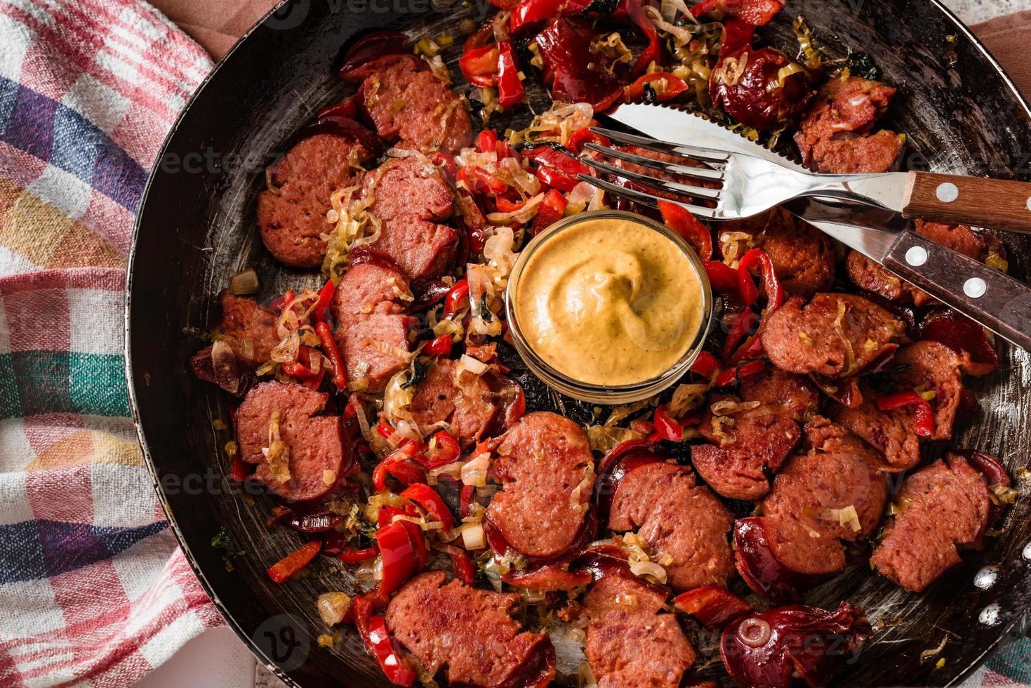 Sliced sausage and mix of fresh vegetables fried in the rustic pan with mustard on dishcloth. photo