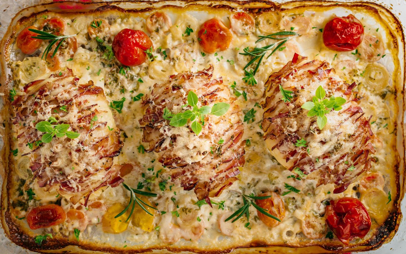 Potato filled with bacon baked in oven. Sour cream for cooking with carrot, tomato, onion, spices and herbs in baking dish. photo