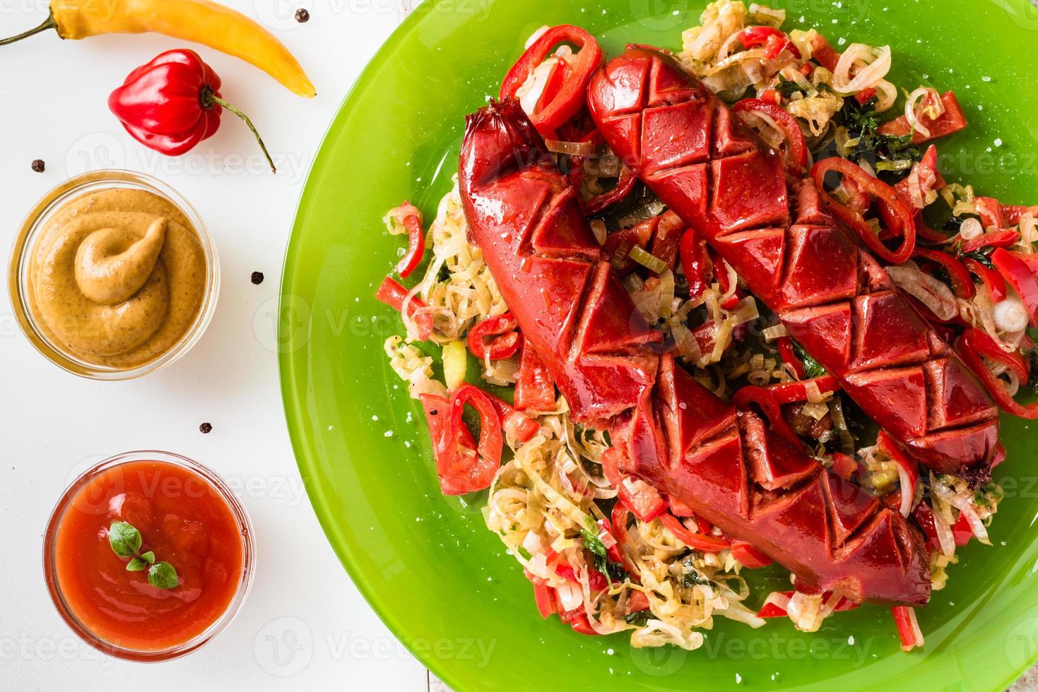 Sausage and mix of fresh vegetables served on a plate, mustard, ketchup, fresh hot chili peppers and herbs. photo
