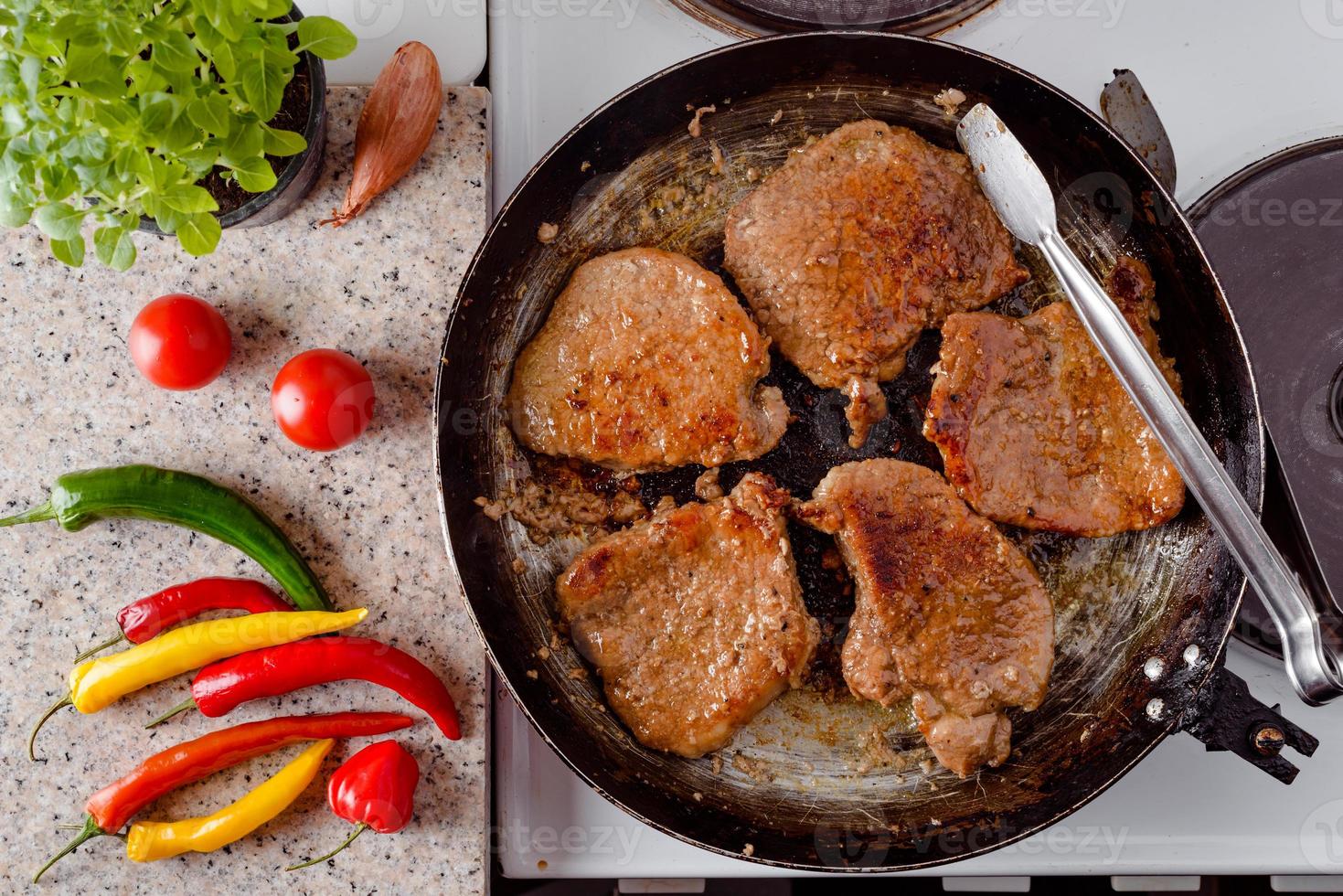 Pork steak roast on rustic pan, fresh hot chili peppers, tomato and herbs. photo