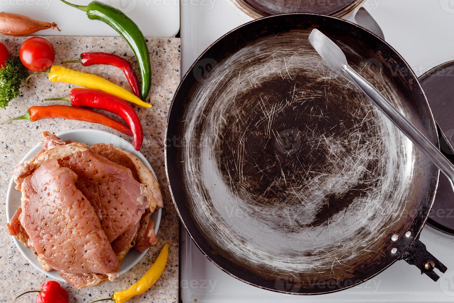 Pork steak ready to be roasted on rustic pan, fresh hot chili peppers, tomato and herbs. photo