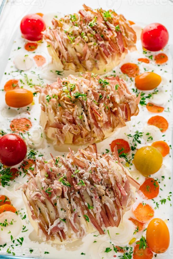 Potato filled with bacon ready to be baked in oven. Sour cream for cooking with carrot, tomato, onion, spices and herbs in baking dish. photo