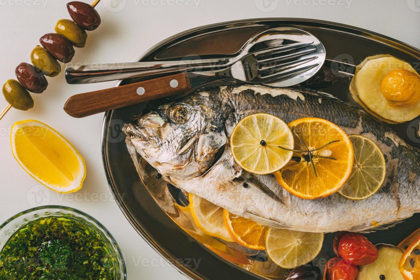 dorada pescado al plato al horno con patatas, romero, limón, naranja, aceitunas, tomates y lima. orata fresca, preparación de pescado dorade. foto