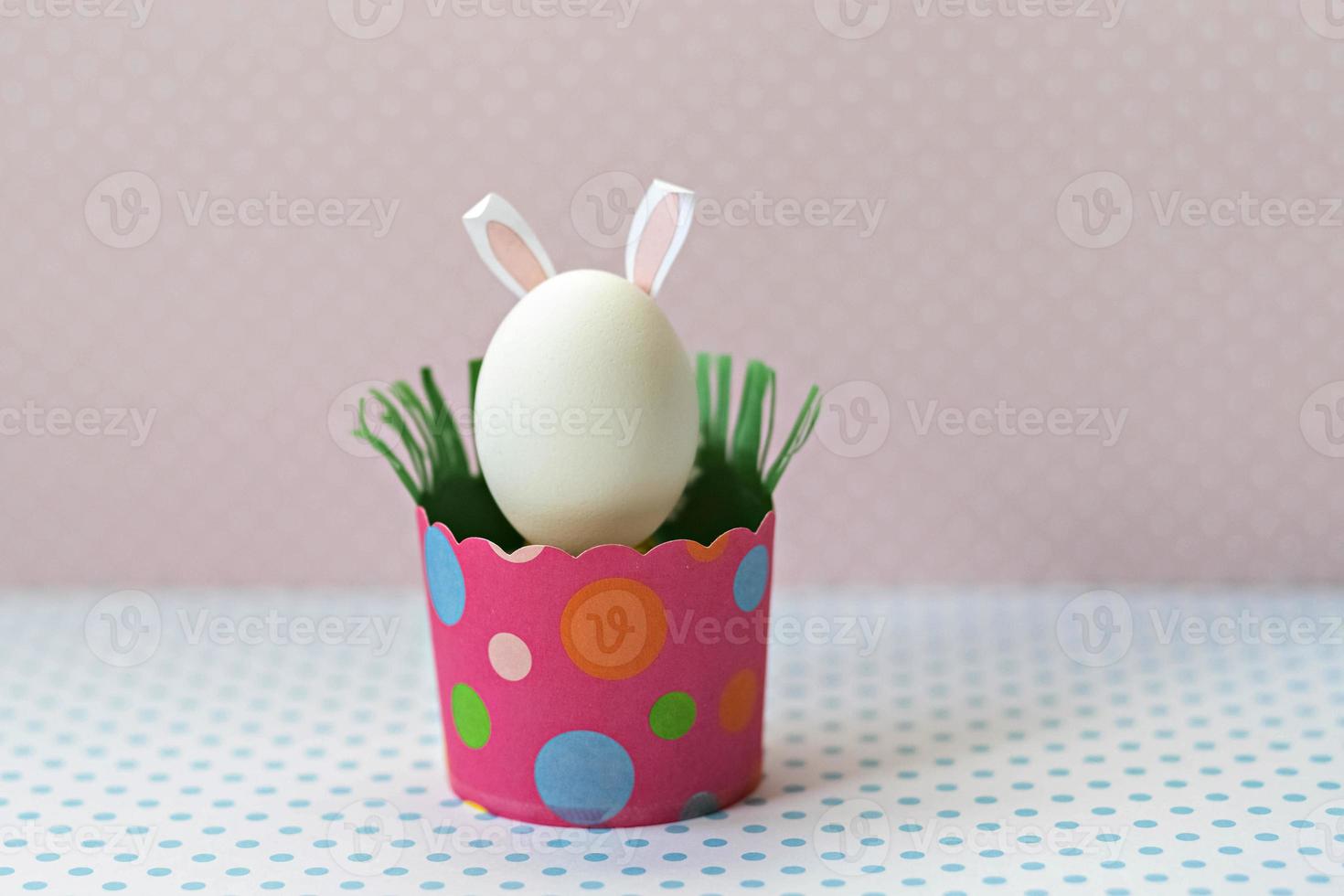 huevo de gallina blanco con orejas de conejo en una bandeja de papel rosa ecológico, caja. feliz concepto de vacaciones de pascua. foto