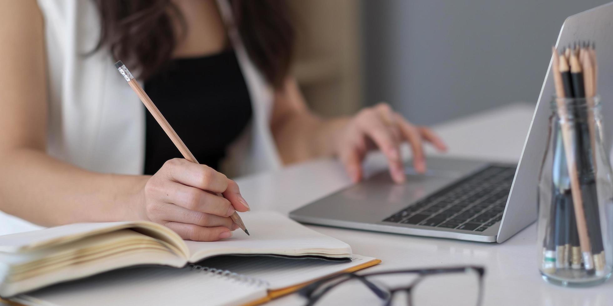 Close up of Asian woman writing on notebook on a table with laptop, girl work at a coffee shop, freelance business concept photo