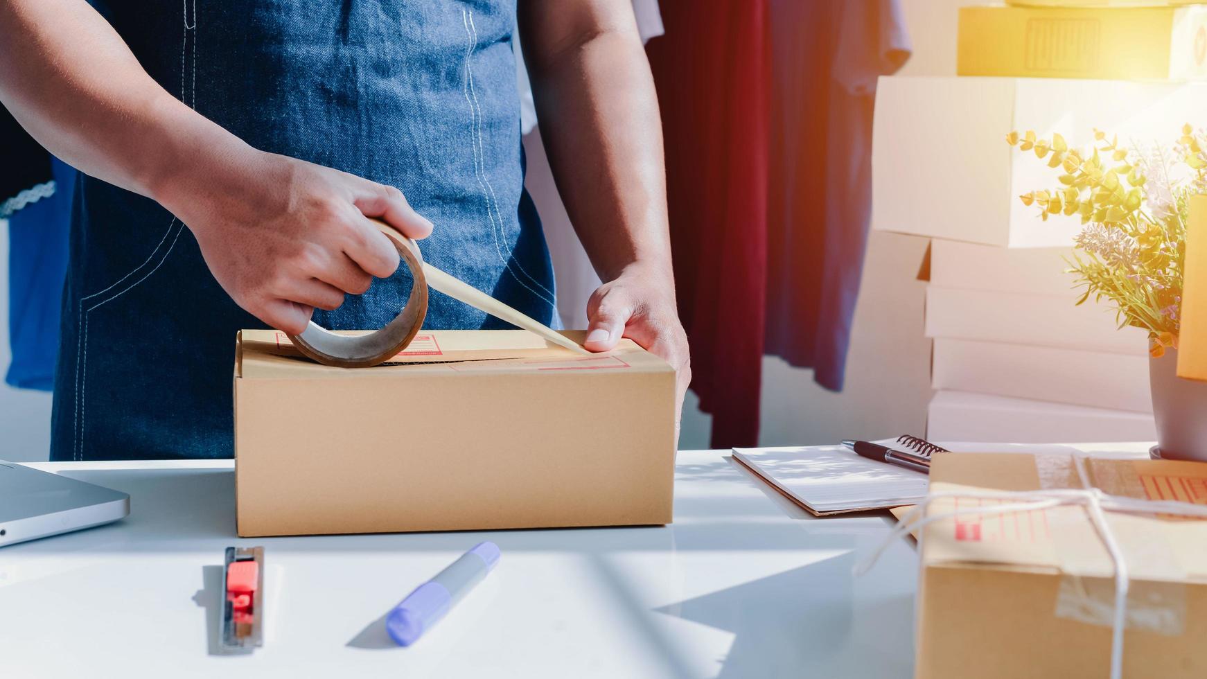 Close-up view of man's online store, small business owner seller, entrepreneur packing package post shipping box preparing delivery parcel on the table, entrepreneurial self-employed business concept photo