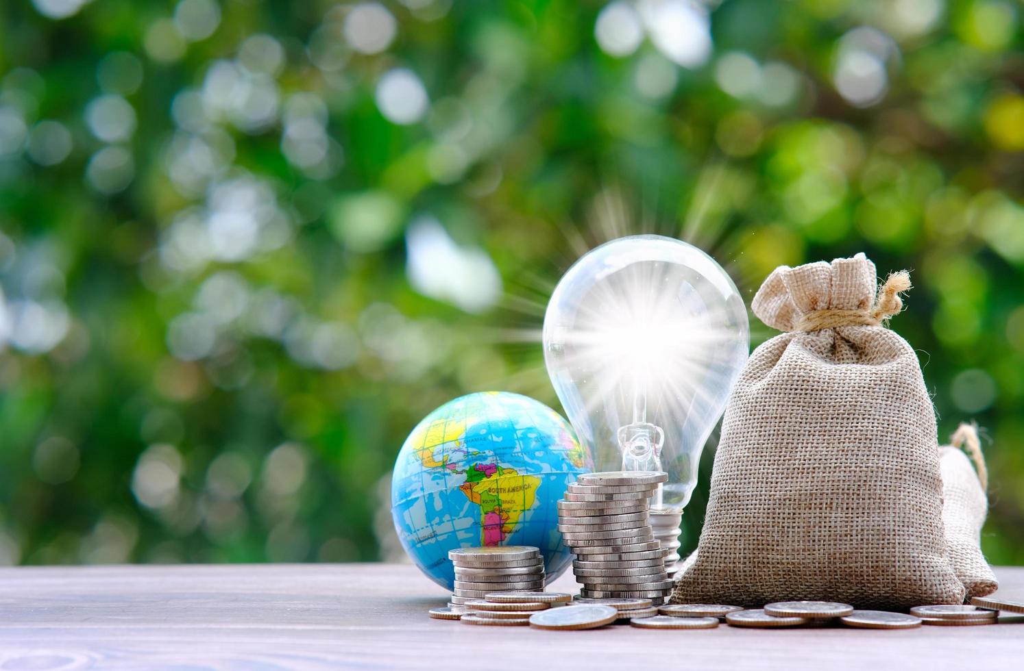 Stacking coins on table with globe on green bokeh background photo