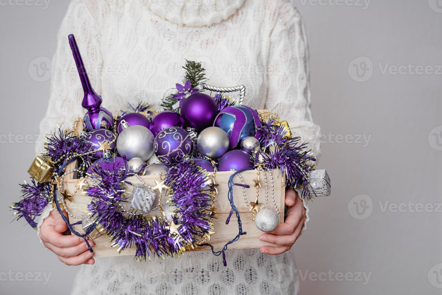 Woman holding a full wooden box of Christmas tree decorations photo
