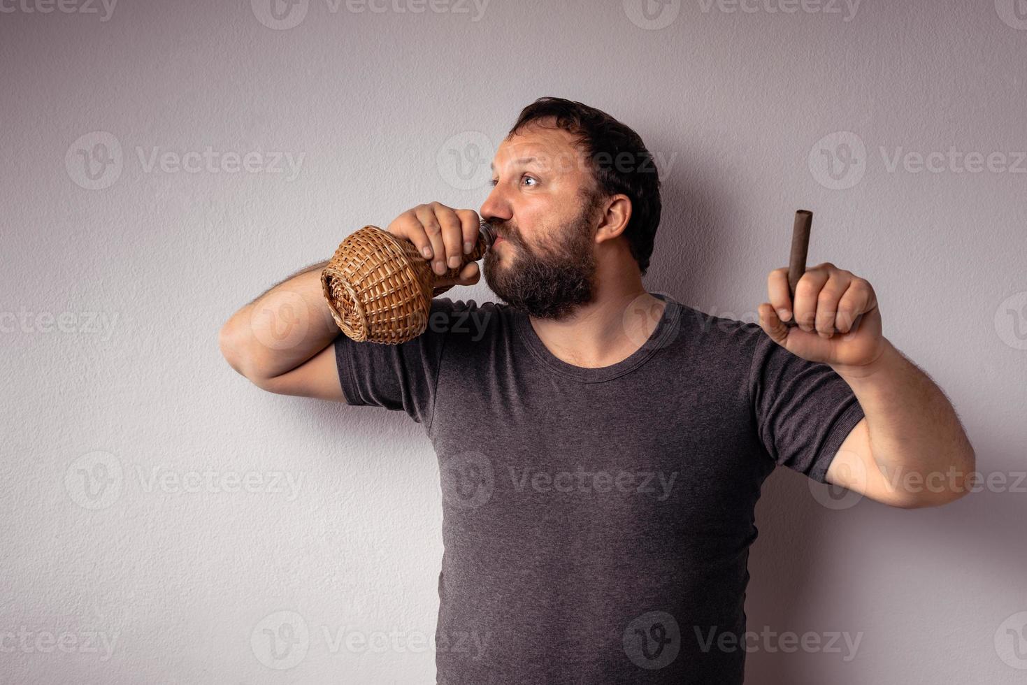 Bearded man drinking from a bottle and holds a cigar and celebrating photo