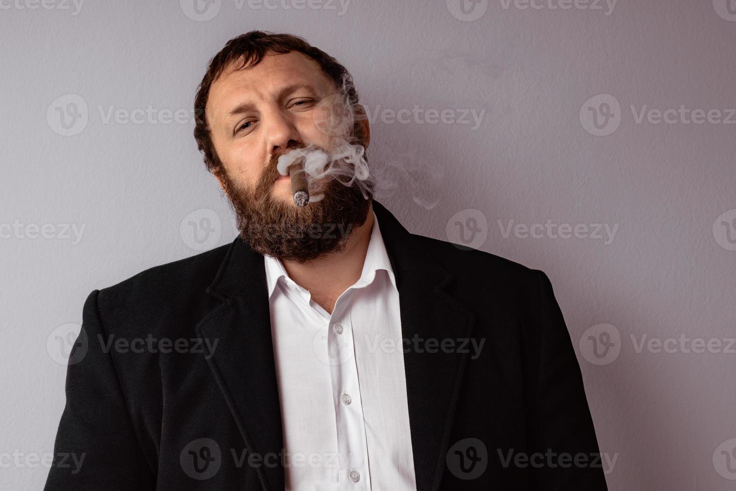 Hombre barbudo en abrigo moderno y camisa fumando su cigarro foto