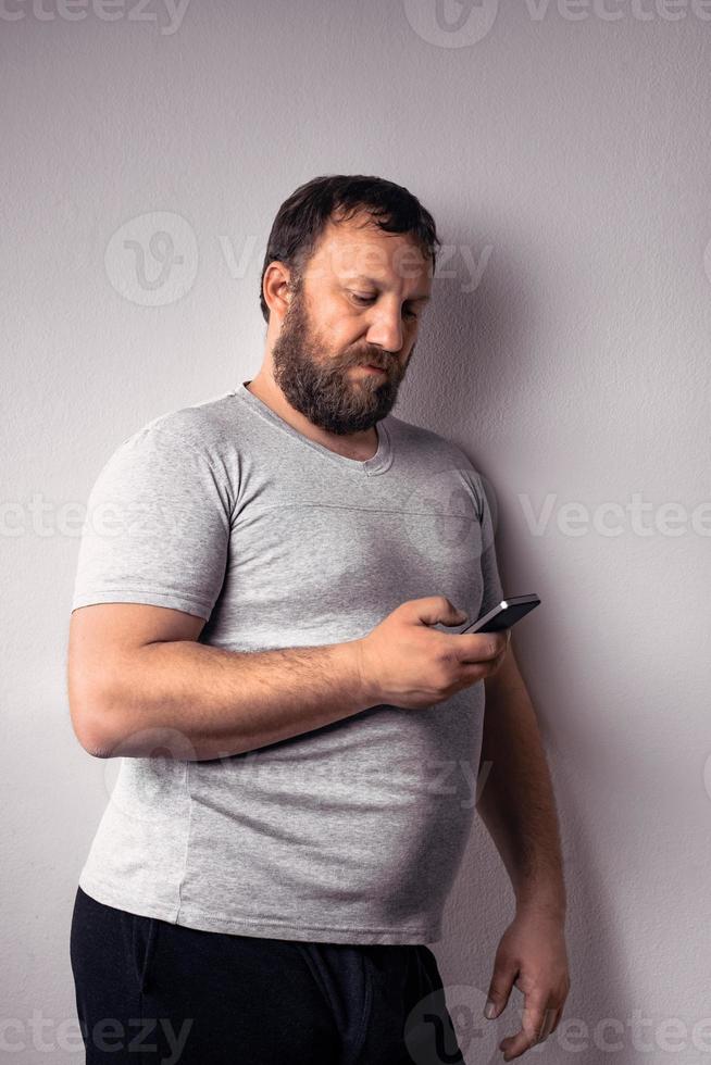 Bearded man in gray t-shirt holding mobile phone photo