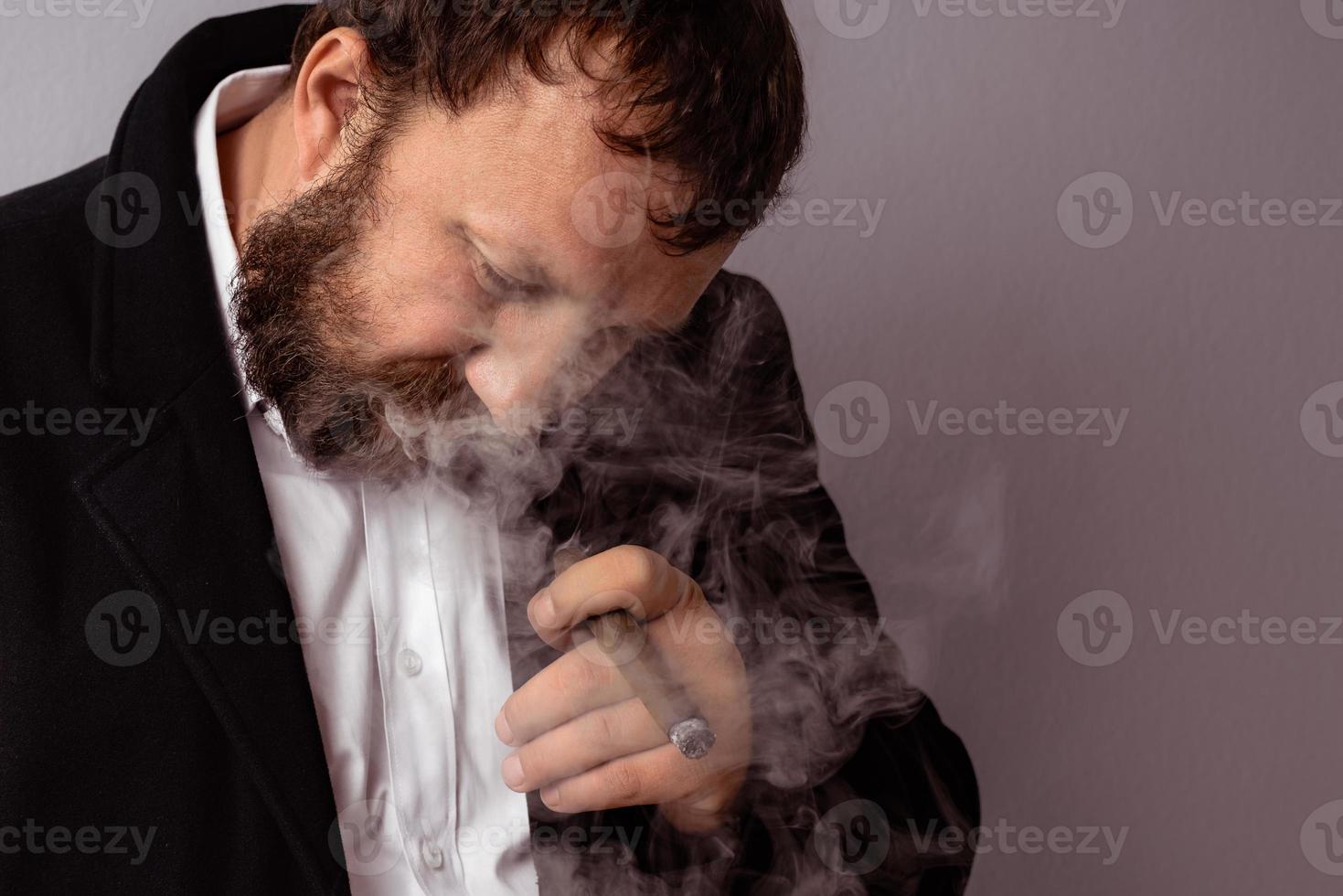 Hombre barbudo en abrigo moderno y camisa fumando su cigarro foto