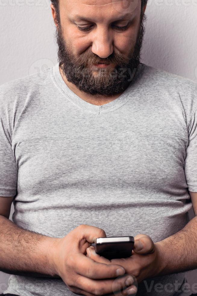 Bearded man in gray t-shirt holding mobile phone photo