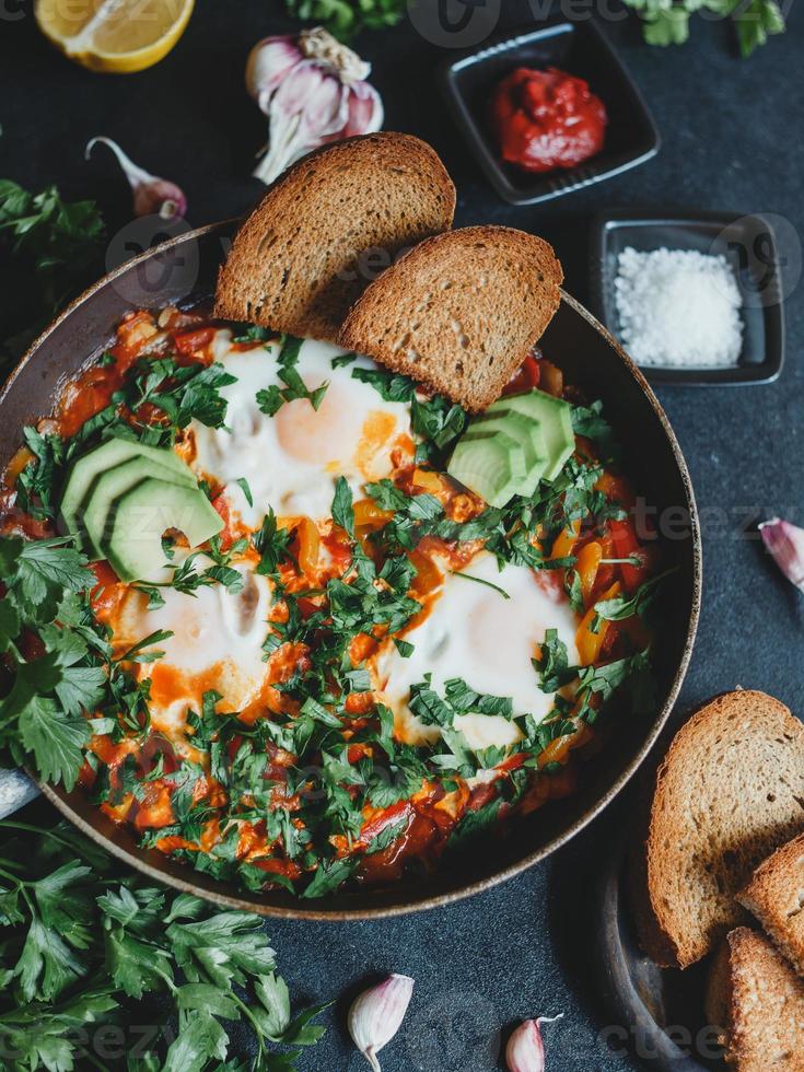 shakshuka con huevos, tomates, pimiento y perejil en una sartén. shakshuka es una comida tradicional israelí. foto