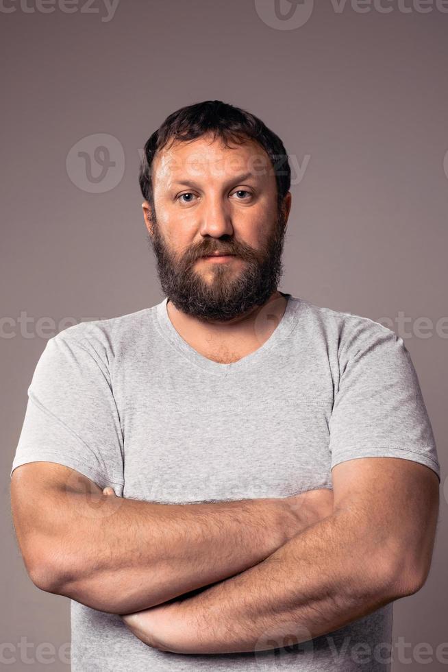 Apuesto hombre barbudo en camiseta gris mirando a la cámara foto