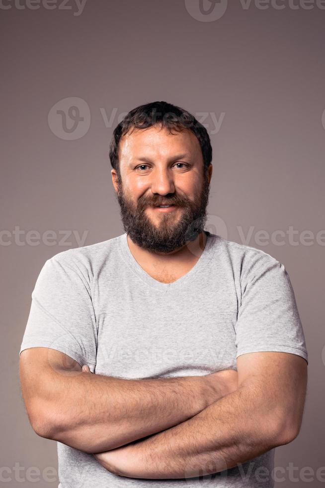 Feliz sonriente chico barbudo en camiseta gris con las manos cruzadas foto