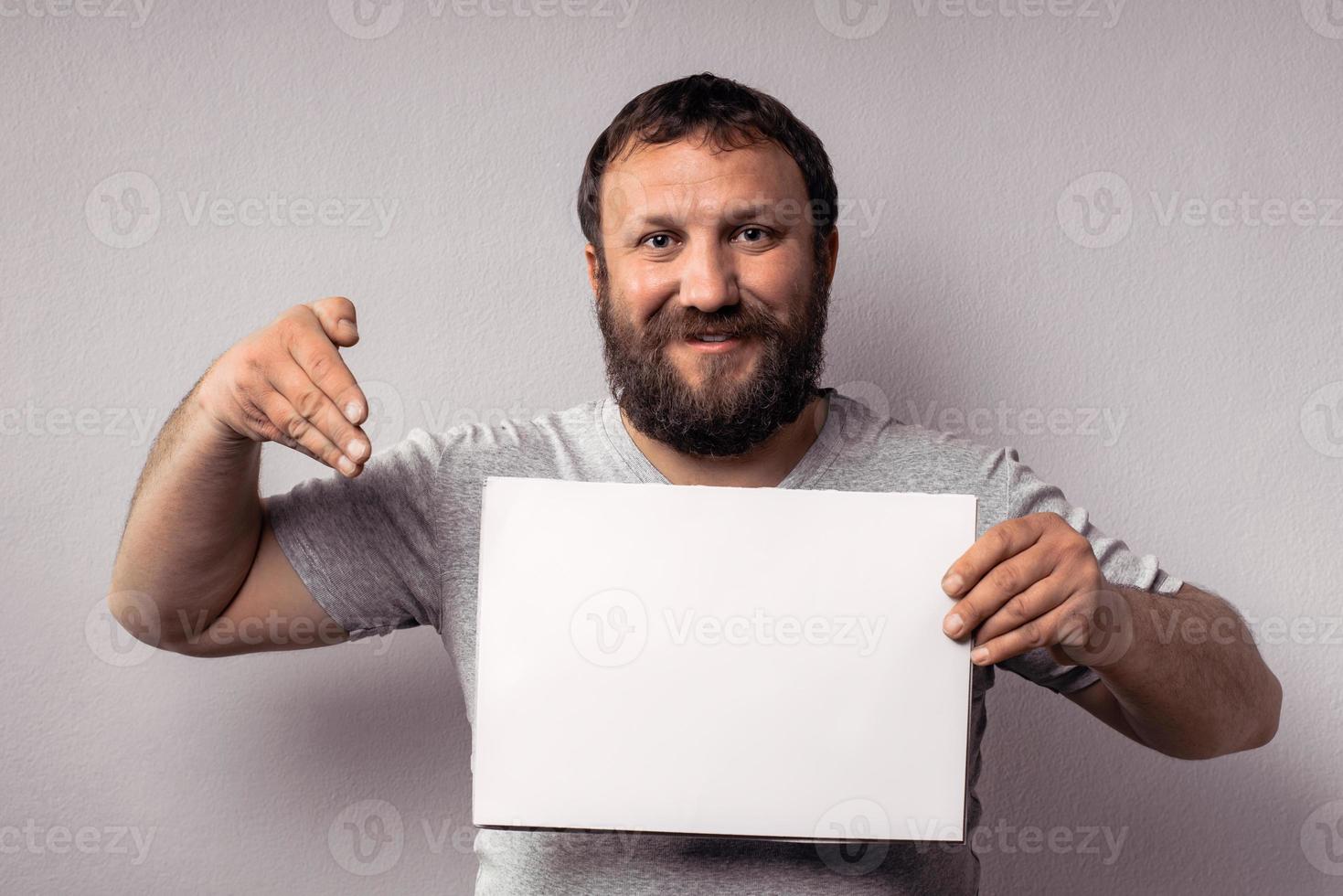 Bearded man in gray t-shirt showing blank white poster photo