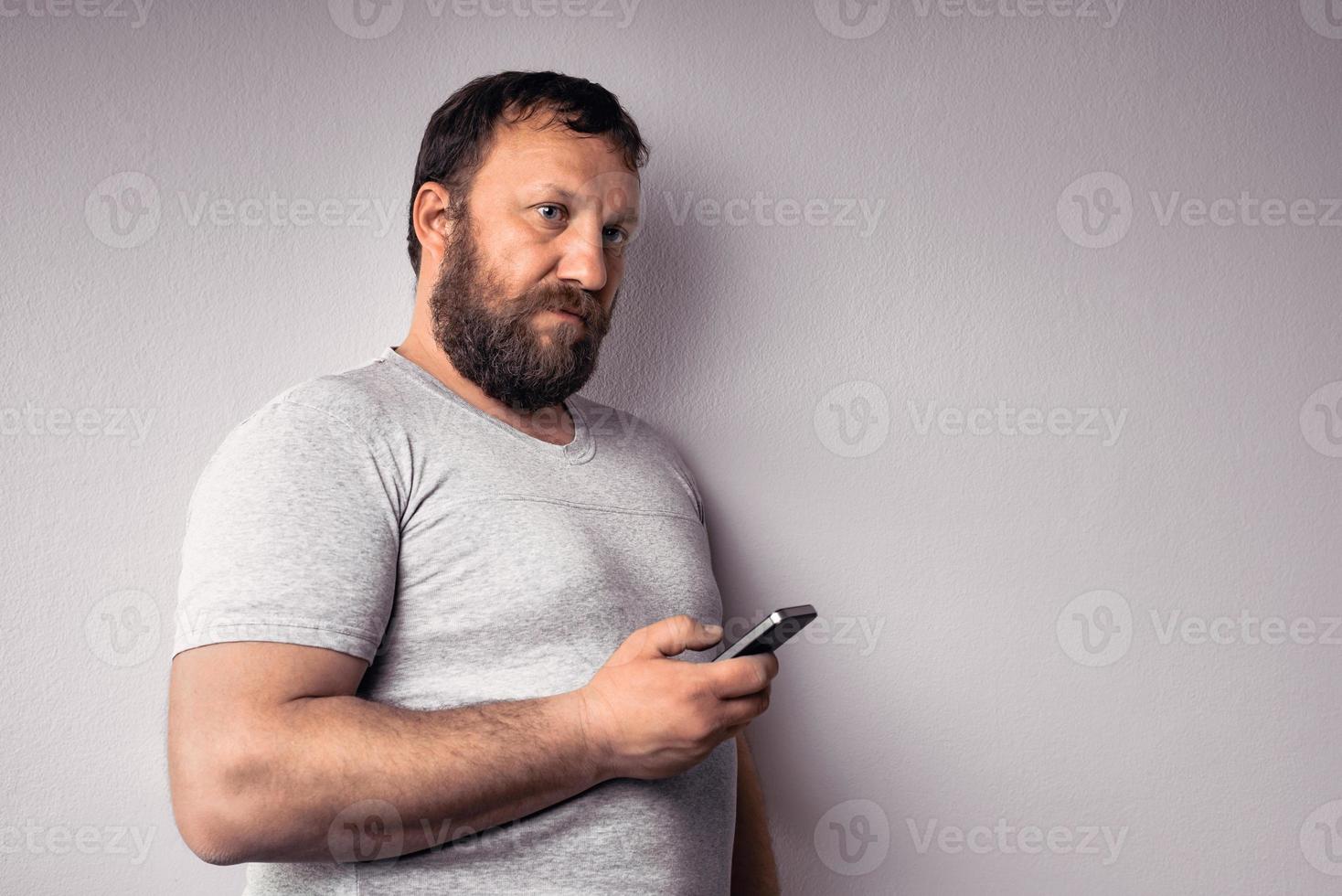 Bearded man in gray t-shirt holding mobile phone photo