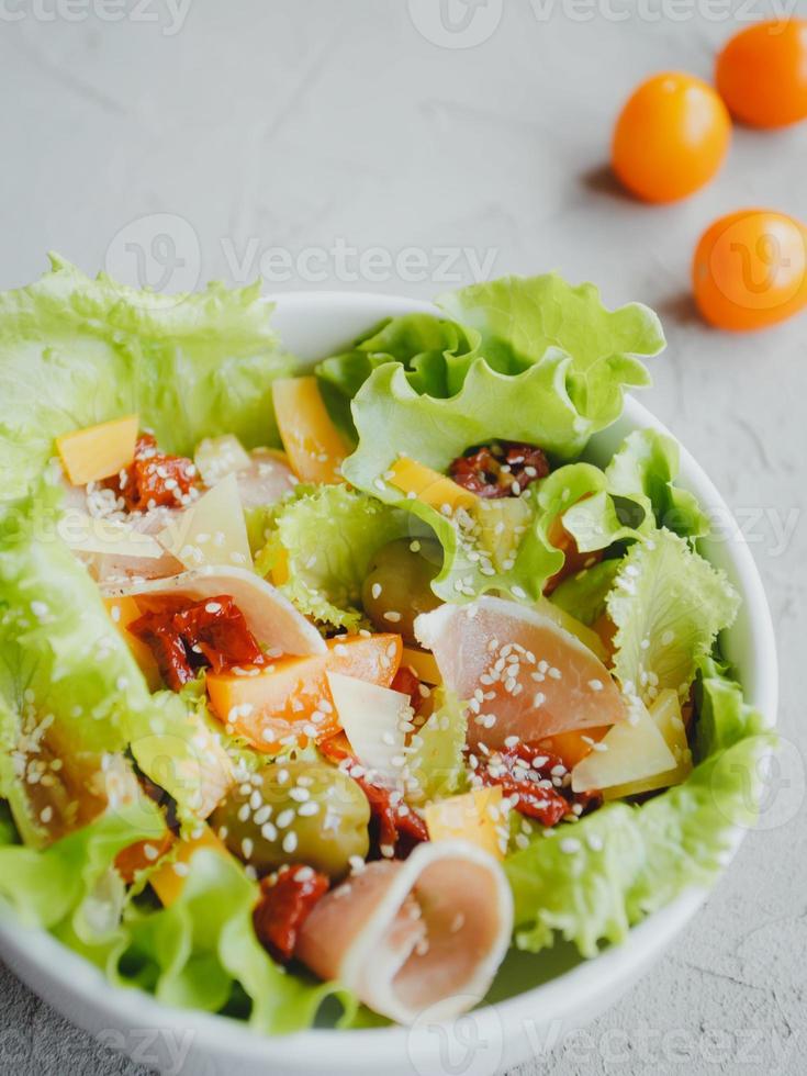 Fresh salad of lettuce, cherry tomatoes, olives, sun-dried tomatoes, Parma ham, cheddar cheese, parmesan, olive oil and sesame. Healthy eating concept. photo