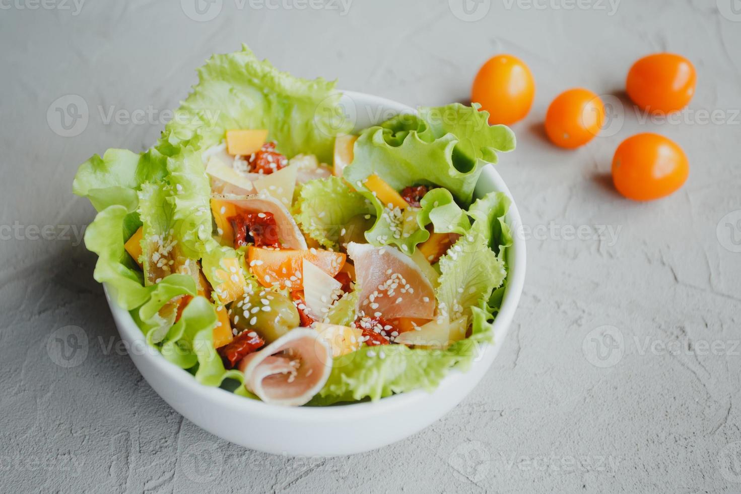 Fresh salad of lettuce, cherry tomatoes, olives, sun-dried tomatoes, Parma ham, cheddar cheese, parmesan, olive oil and sesame. Healthy eating concept. photo