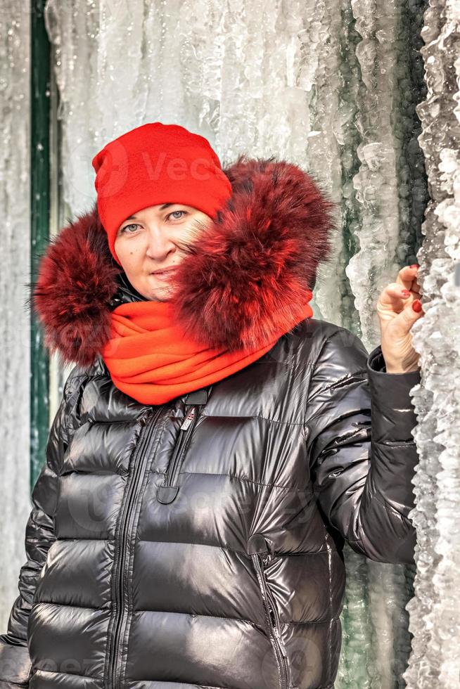 Portrait of a woman in a red hat and scarf, warm jacket against the background of an ice wall. Winter photo