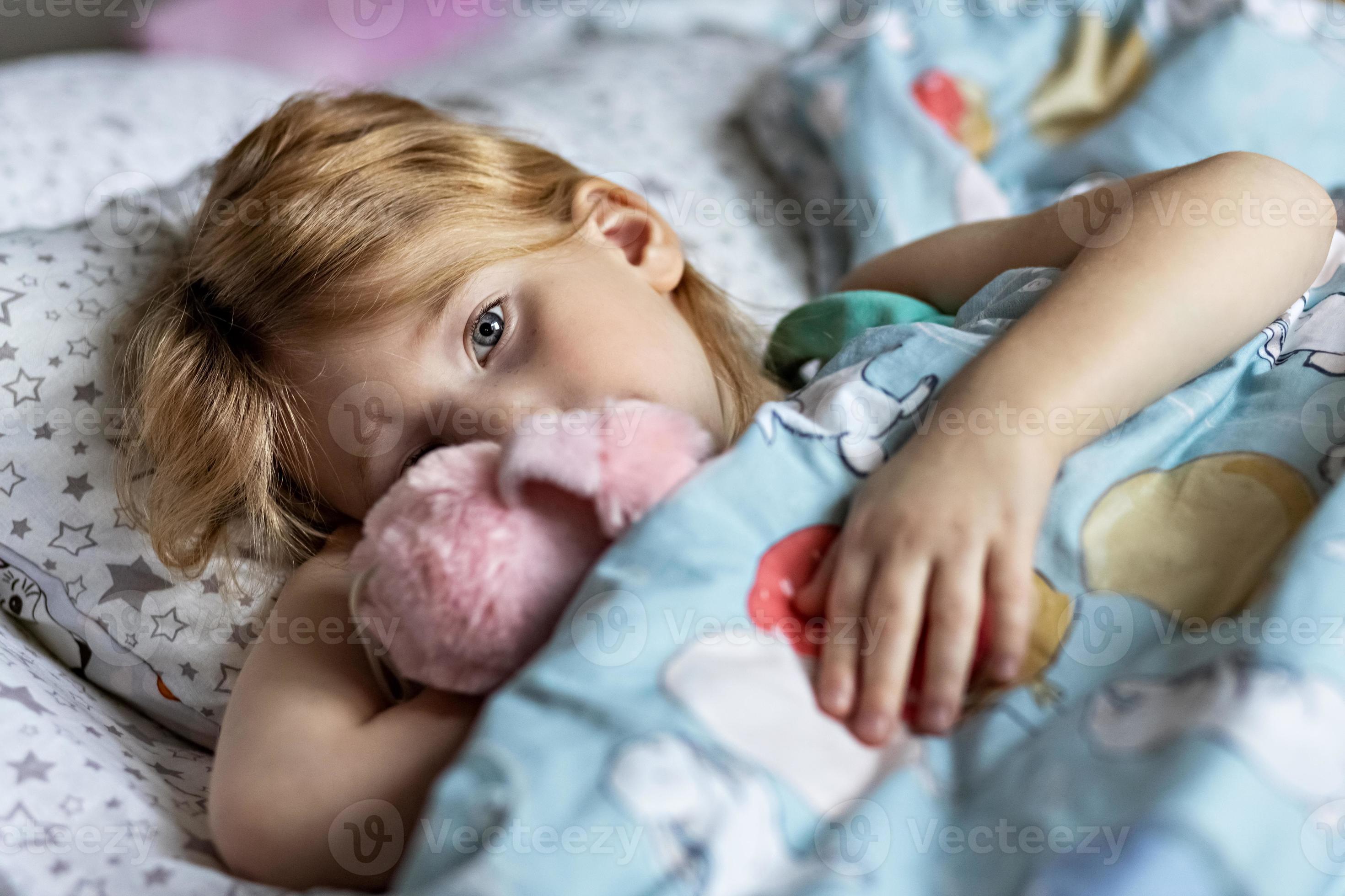 A little girl lies under a blanket with a toy dog getting ready for bed