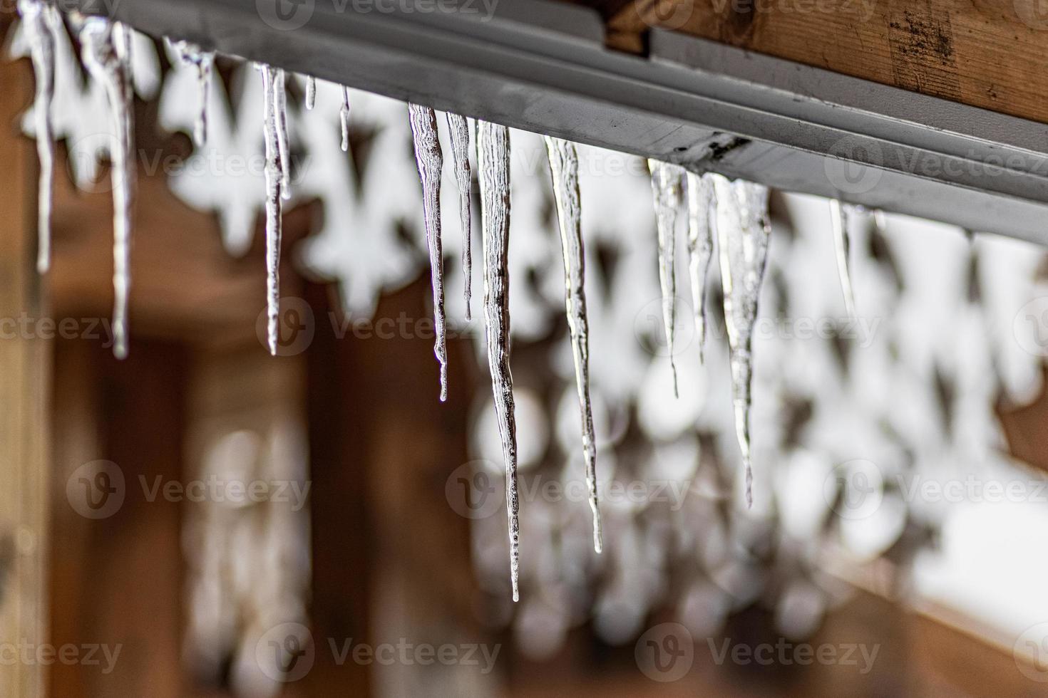 A large transparent ice icicle hangs from the roof of the house. Winter frosts photo