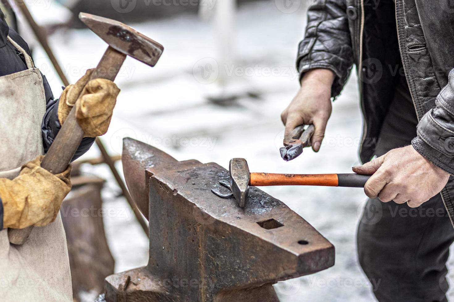 A blacksmith man and his son forge a horseshoe on an anvil. photo