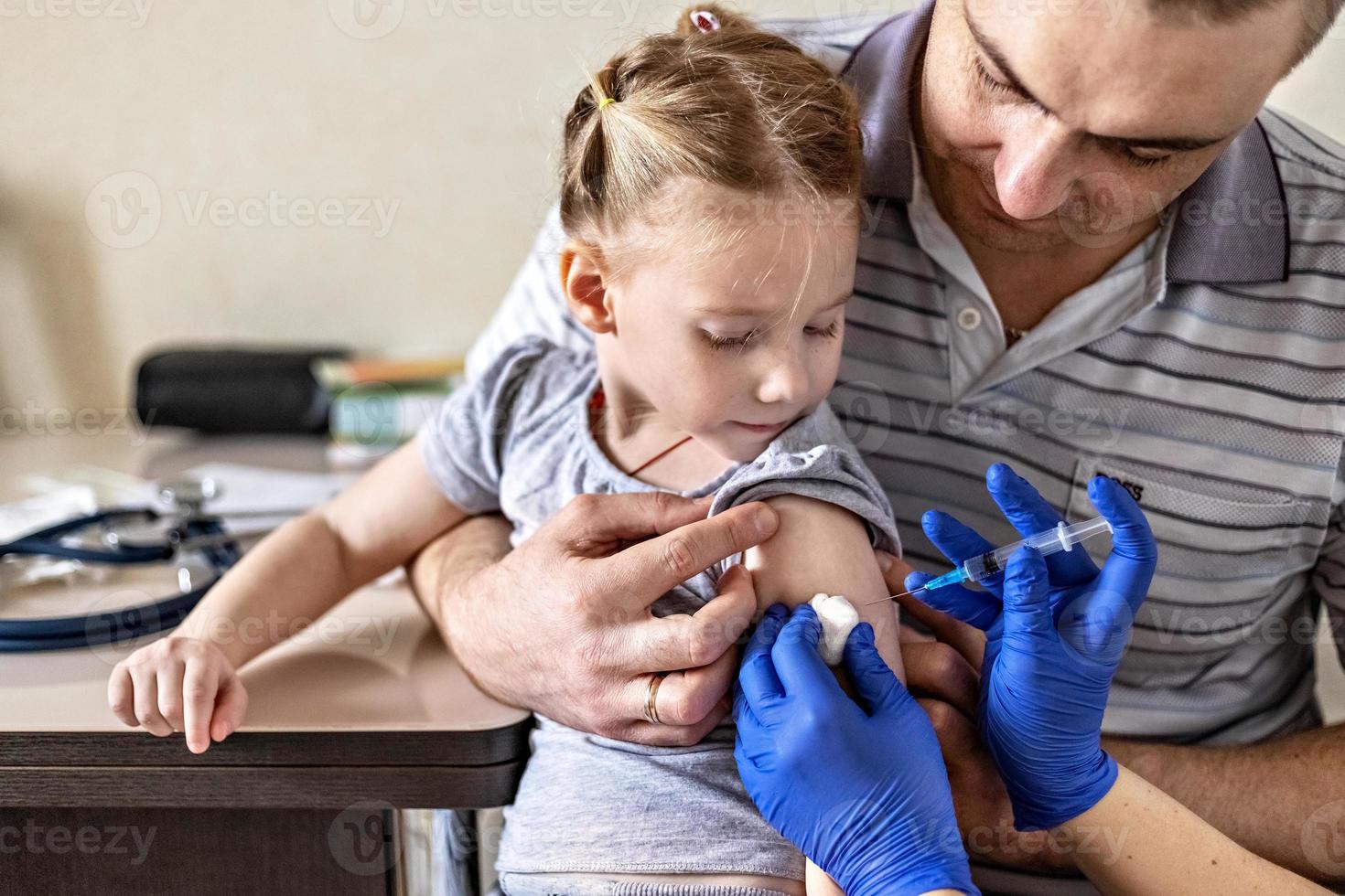 una niña con su padre en el consultorio del médico de la clínica está siendo vacunada contra el coronavirus. el concepto de vacunación, inmunización, prevención contra covid-19. foto