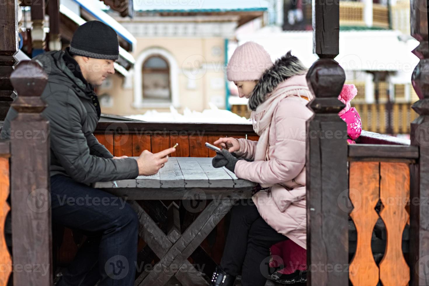 una pareja está esperando su pedido para el almuerzo en un café de la calle, enviando mensajes de texto por teléfono. comunicación con personas en un teléfono inteligente. foto