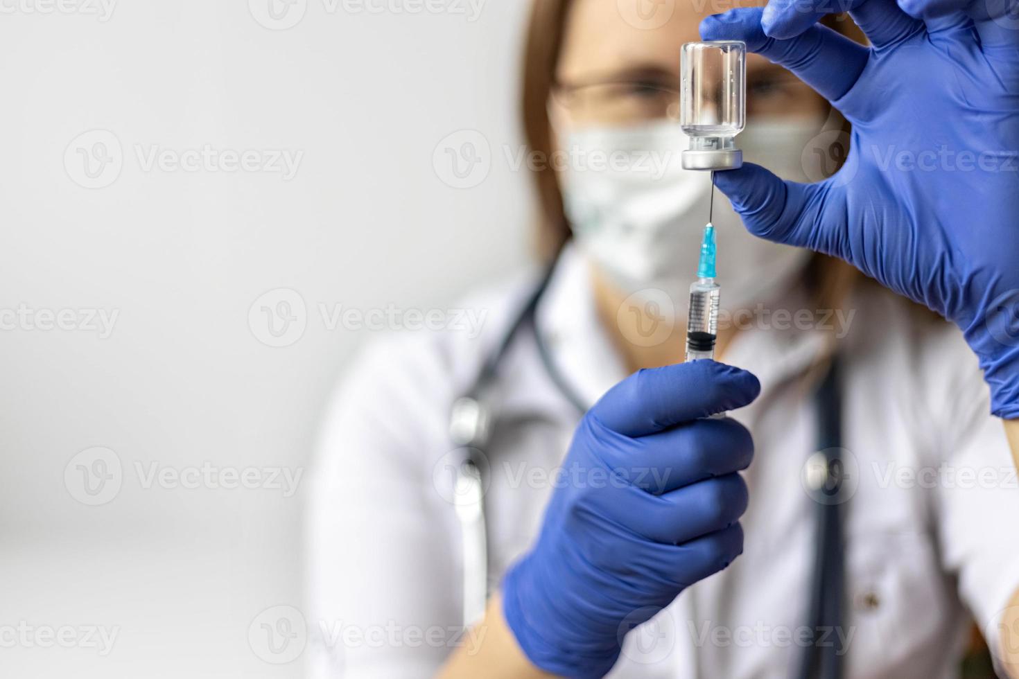 A female doctor wearing a medical mask draws the coronavirus vaccine into a syringe at the clinic.The concept of vaccination, immunization, prevention against Covid-19. photo