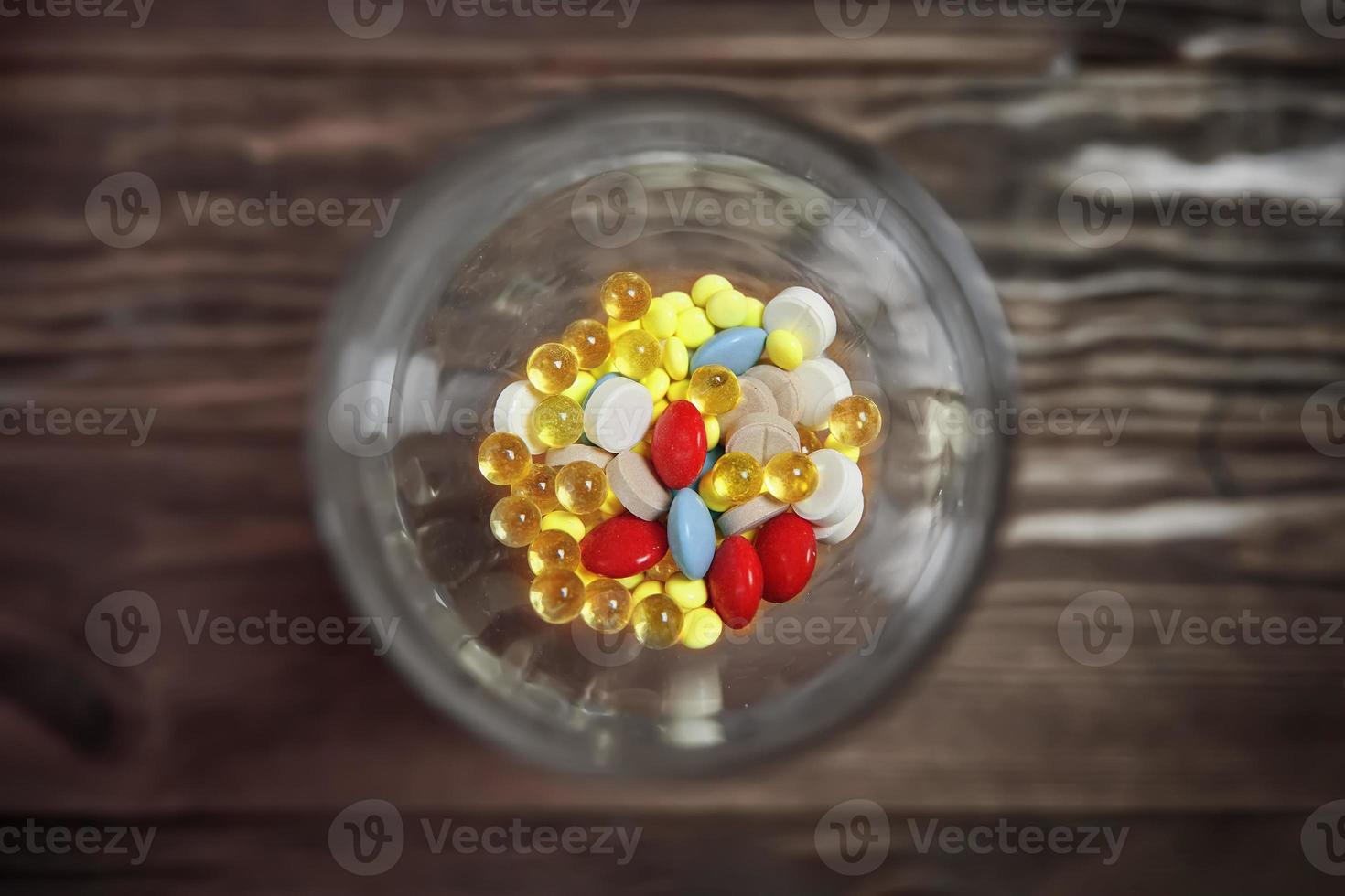 Flat lay of glass with colorful vitamins and pills inside. photo