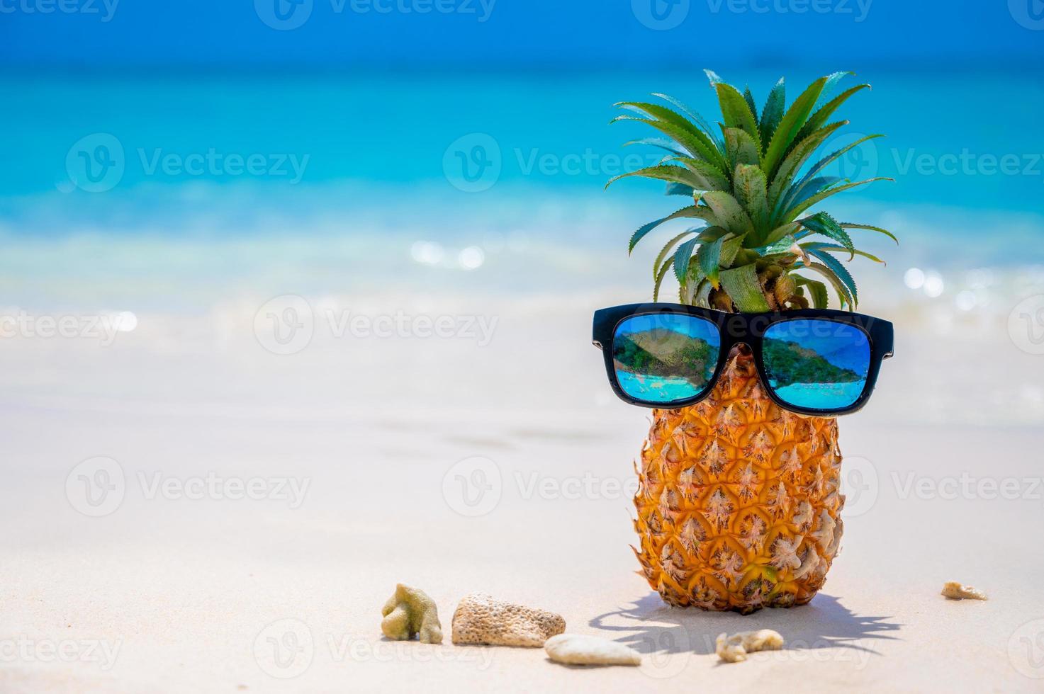 Glasses pineapples are located on the beach by the sea in the hot sun, setting the concept for summer. photo