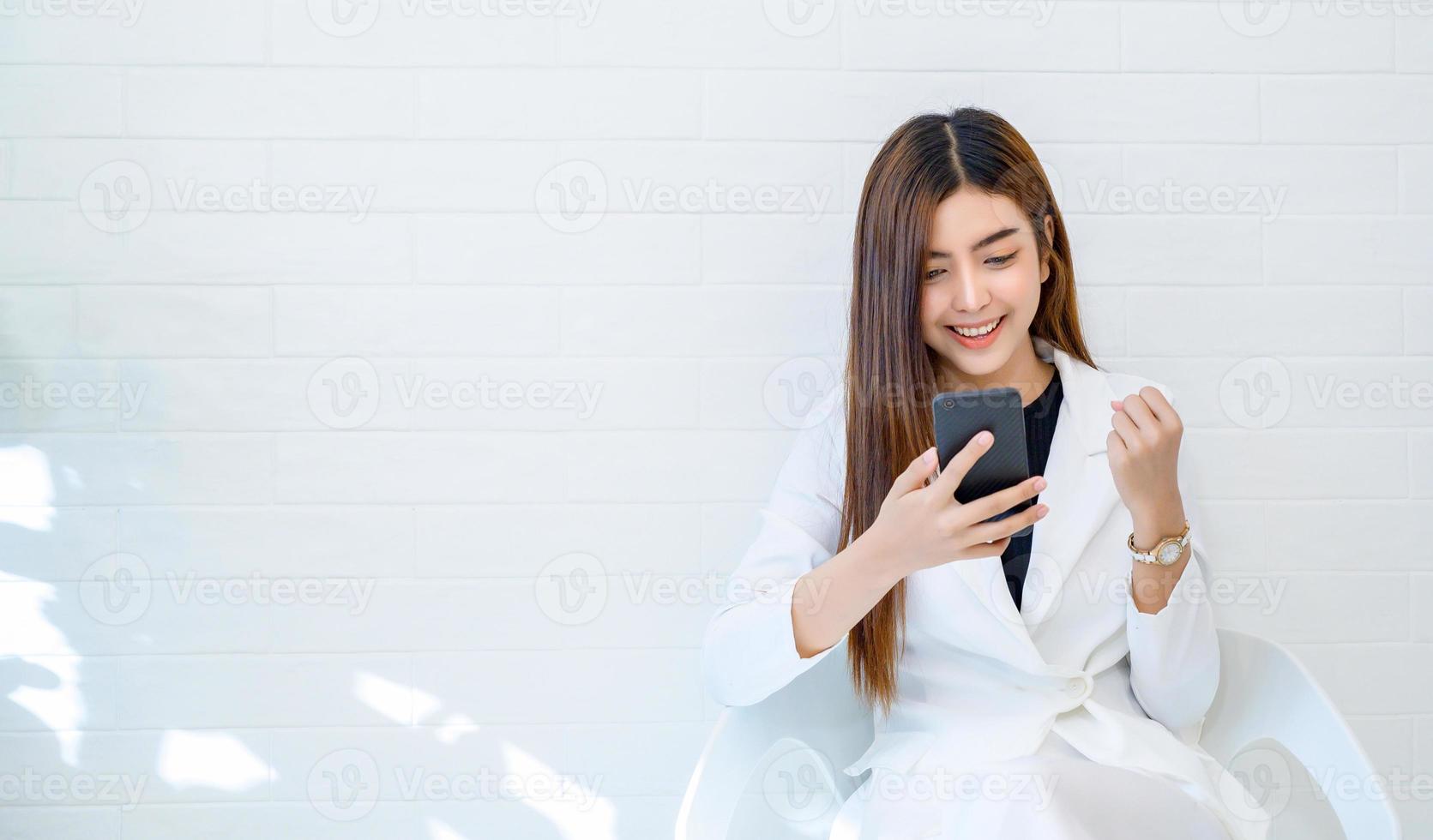 Las mujeres de negocios visten ropa blanca feliz de jugar el teléfono móvil en un fondo blanco. foto