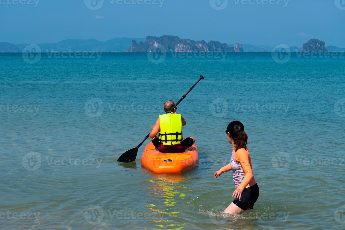 asian senior father playing standing up paddleboard or SUP with young daughter at blue sea on summer vacation. family together concept photo