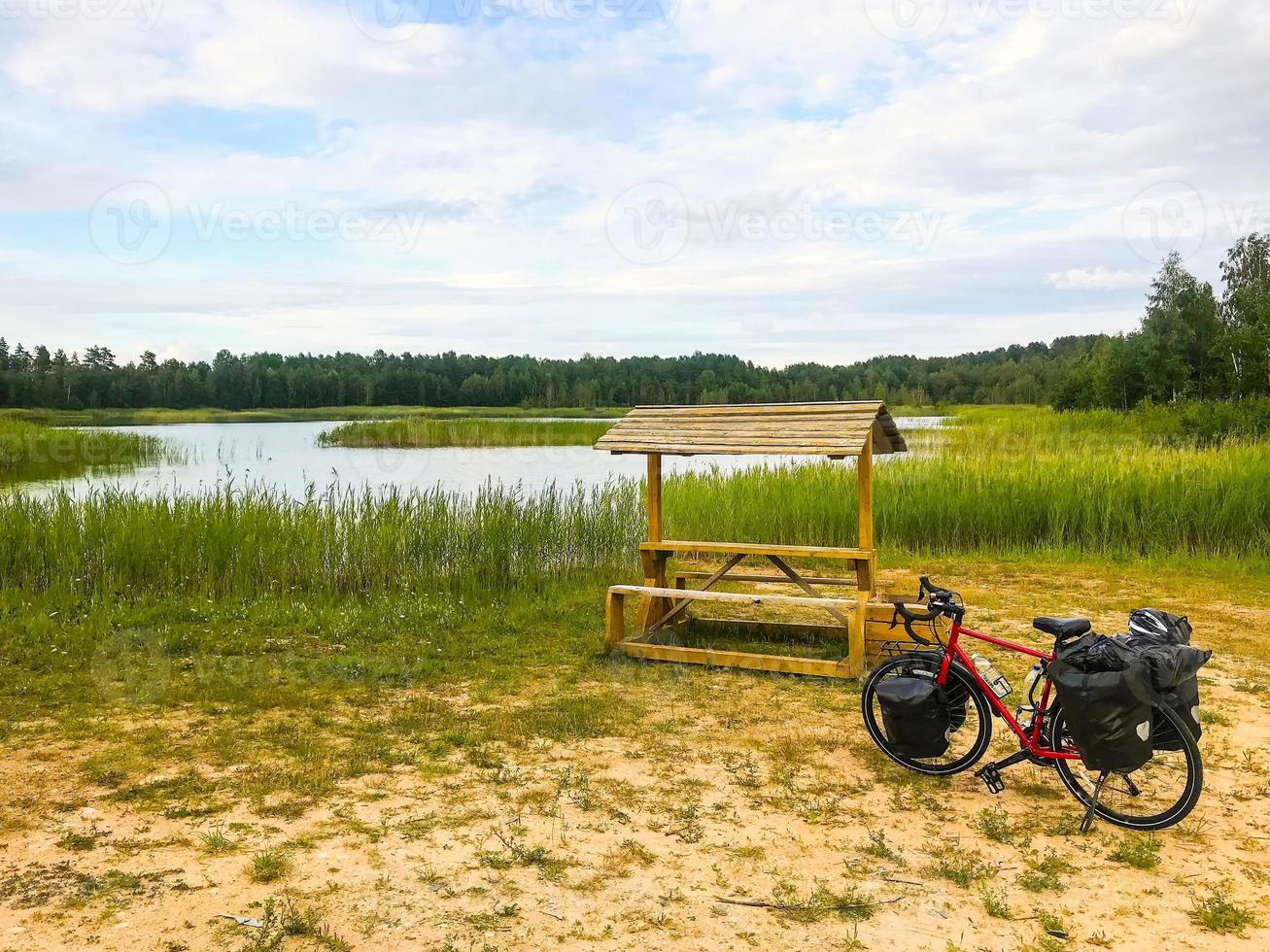 Bicicleta de turismo completamente cargada de pie junto a la mesa de madera con fondo del lago. Bicicleta de turismo en la campiña de Lituania. foto