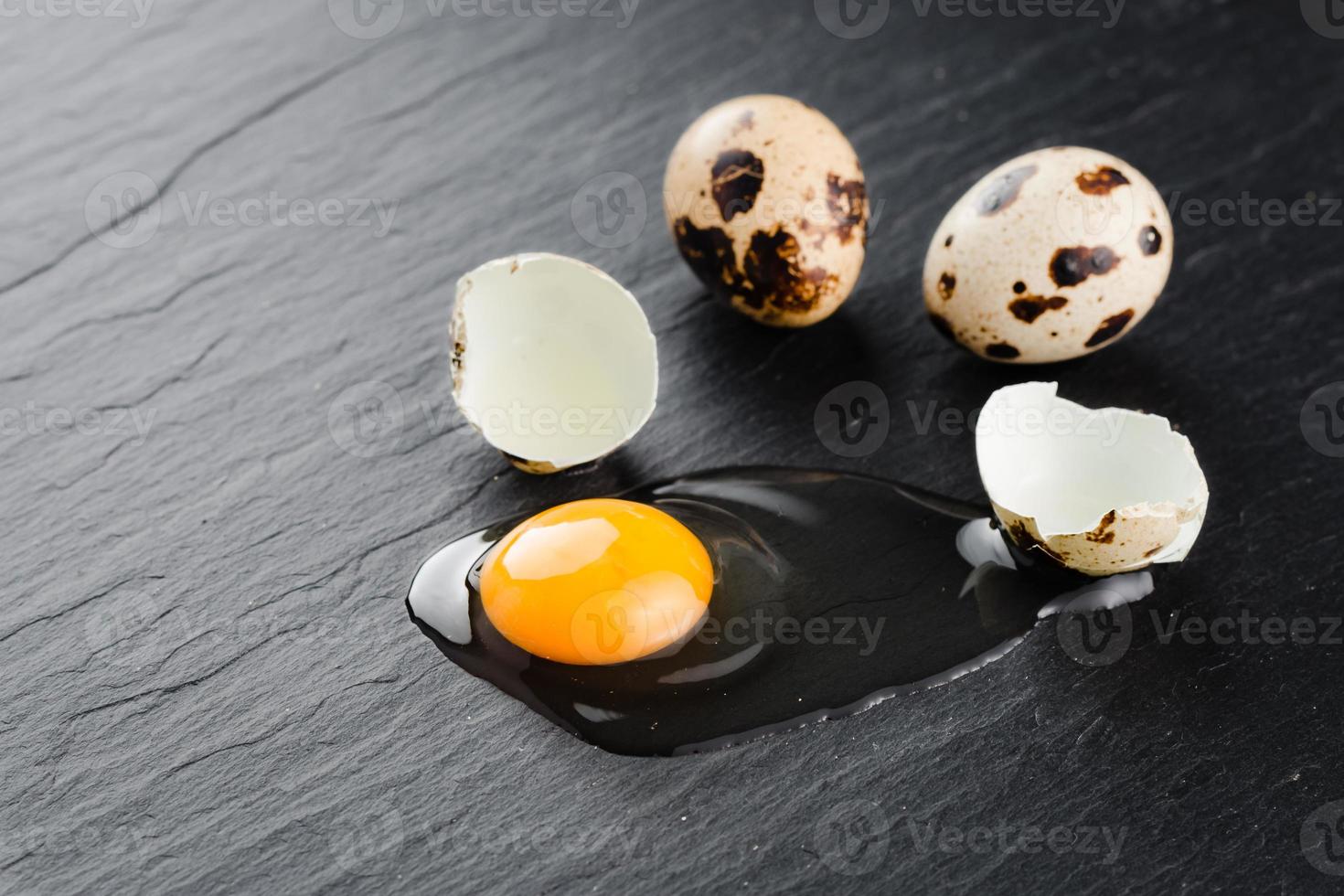 Quail eggs on black stone background, broken, cracked quail egg, yolk of quail egg. Organic product. photo