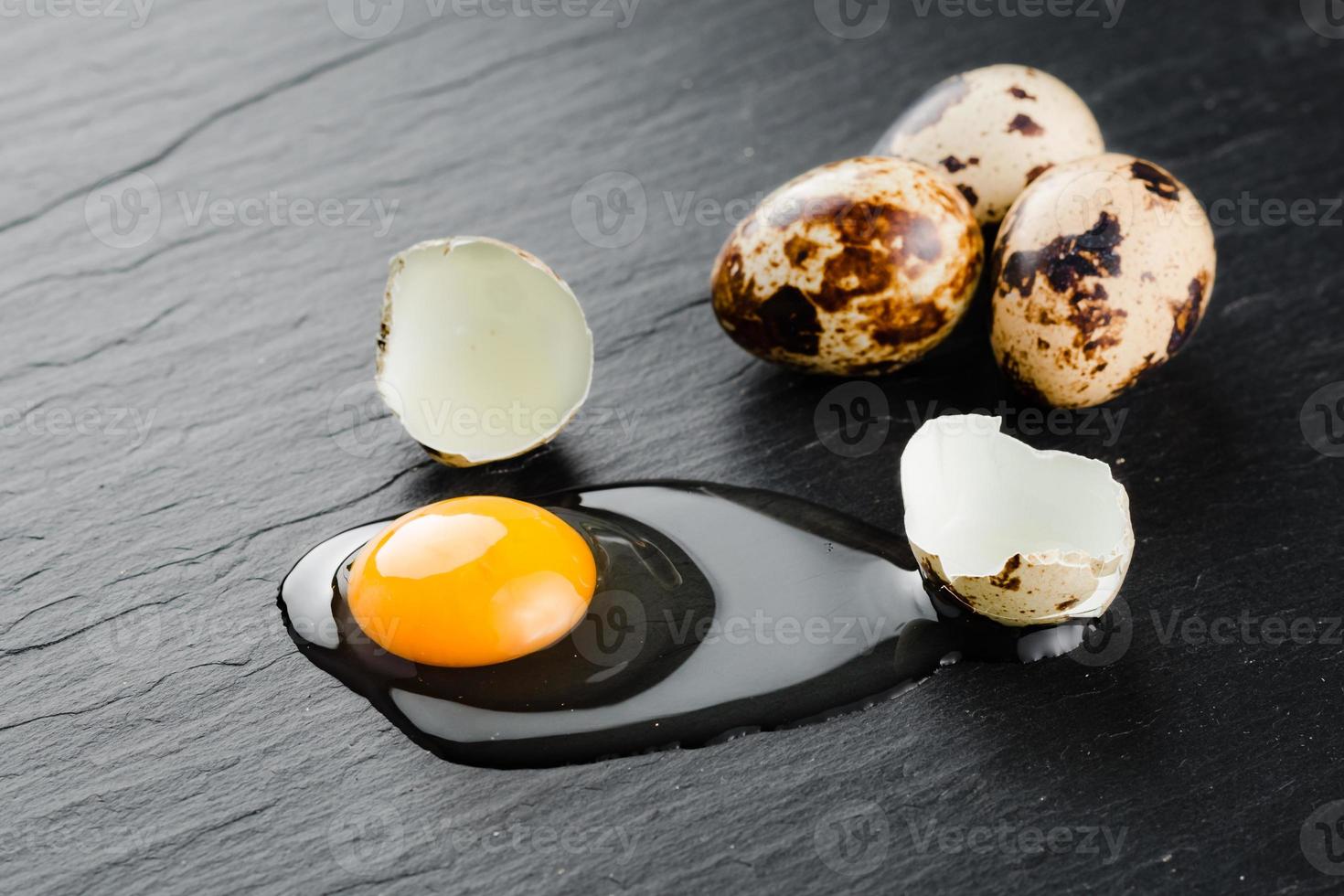 Quail eggs on black stone background, broken, cracked quail egg, yolk of quail egg. Organic product. photo