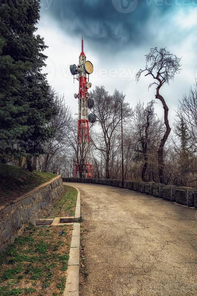 torre de televisión junto a la carretera asfaltada, cielo espectacular, antiguo camino rural de montaña forestal con valla de piedra. foto