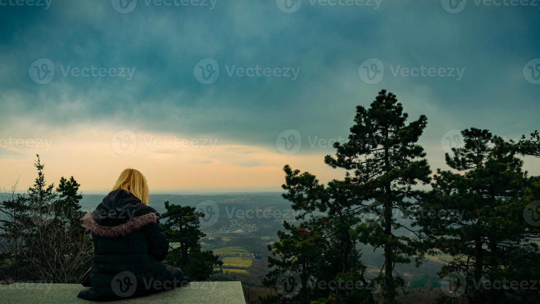 A woman sitting on the edge of forest gate, enjoying the beautiful sunset view, mountain panoramic landscape view. photo